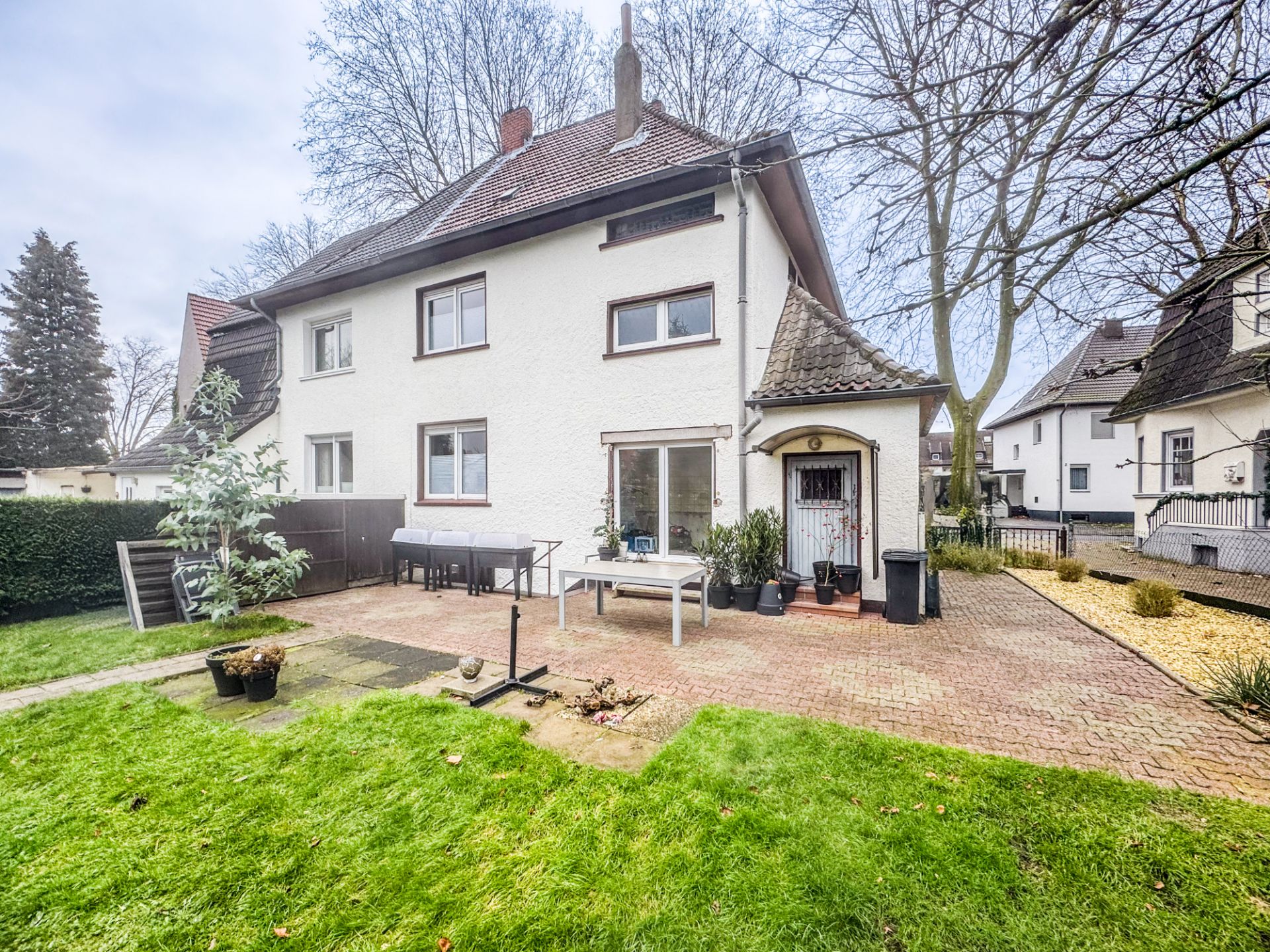 Hinteransicht eines weißen Wohnhauses mit Terrasse, Gartenmöbeln und Grünfläche.