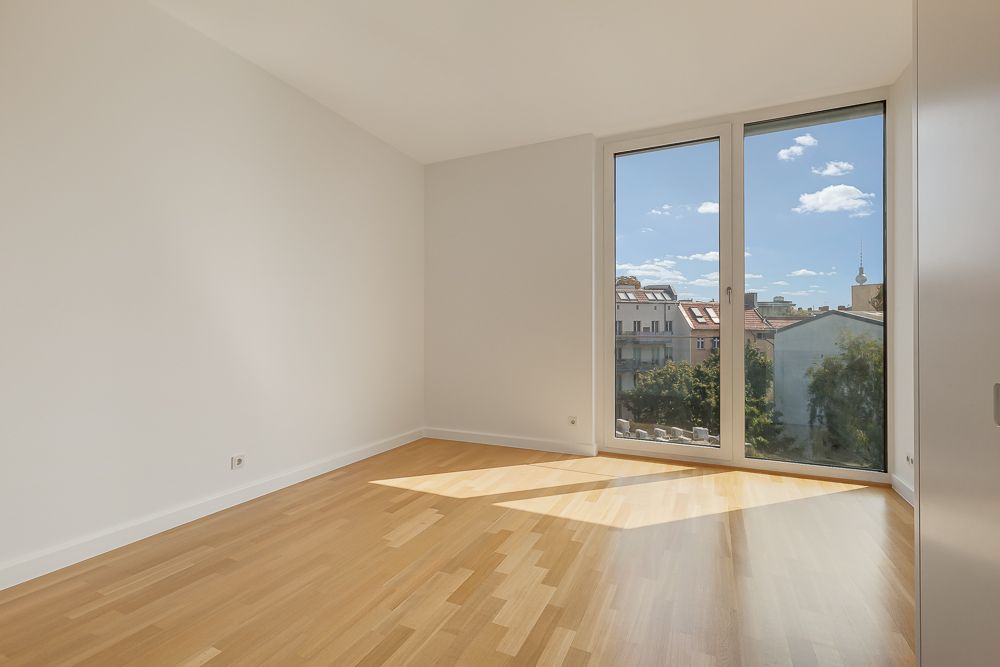 Leerer, heller Raum mit Holzfußboden und großen Fenstern mit Blick auf Stadt und Himmel.