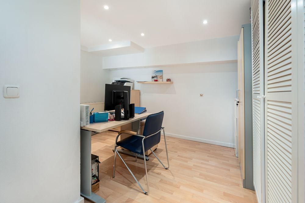 Helles Arbeitszimmer mit Schreibtisch, Stuhl, Computer und Regalen auf Parkettboden.