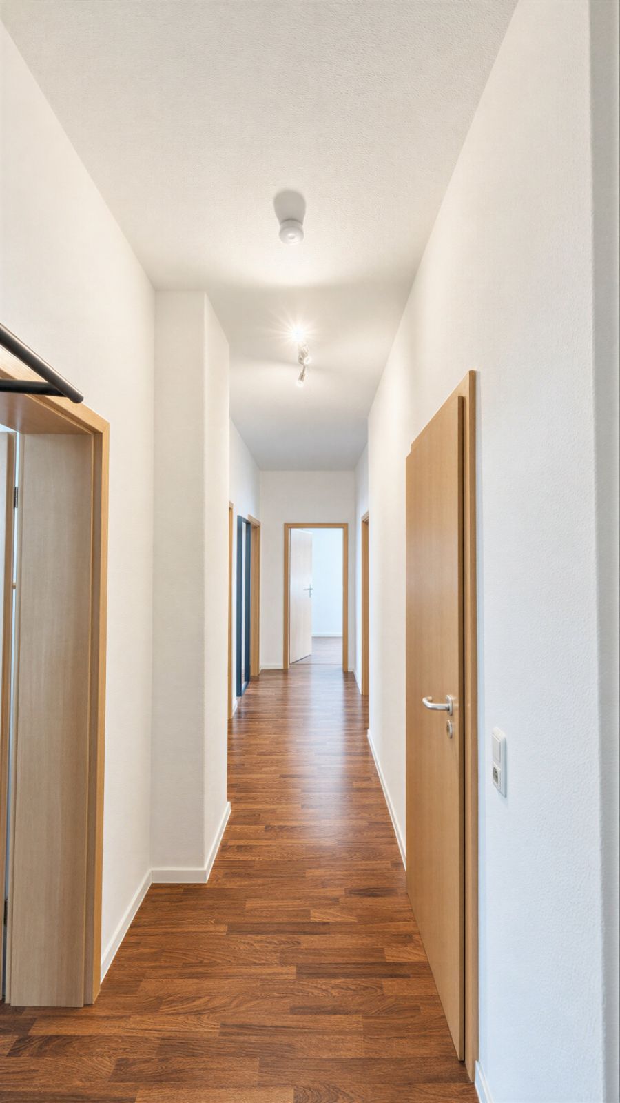Heller Flur mit Holzboden, weißen Wänden und mehreren offenen Türen in einer Wohnung.