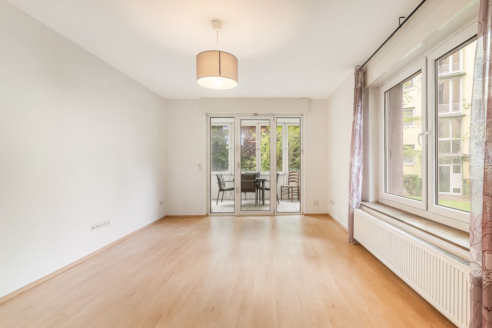 Helles Wohnzimmer mit Holzboden, Fensterfront und Zugang zu einer Terrasse mit Sitzmöbeln.