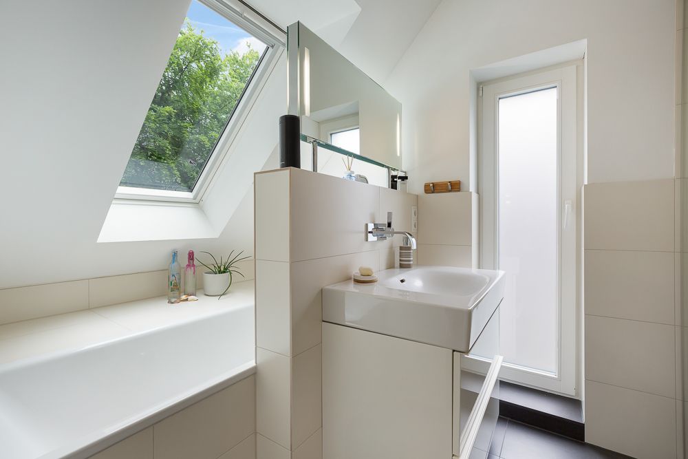 Helles Badezimmer mit Waschbecken, Badewanne, großem Fenster und Spiegel.