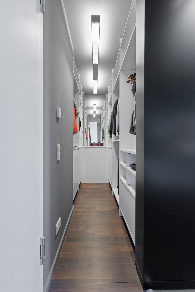 Moderner, schmaler begehbarer Kleiderschrank mit Regalen, Kleidung und Holzfußboden.