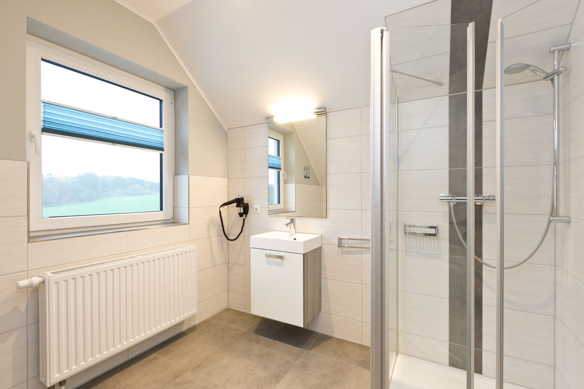 Modernes Badezimmer mit Dusche, Waschbecken, Spiegel, Fenster und Heizkörper.