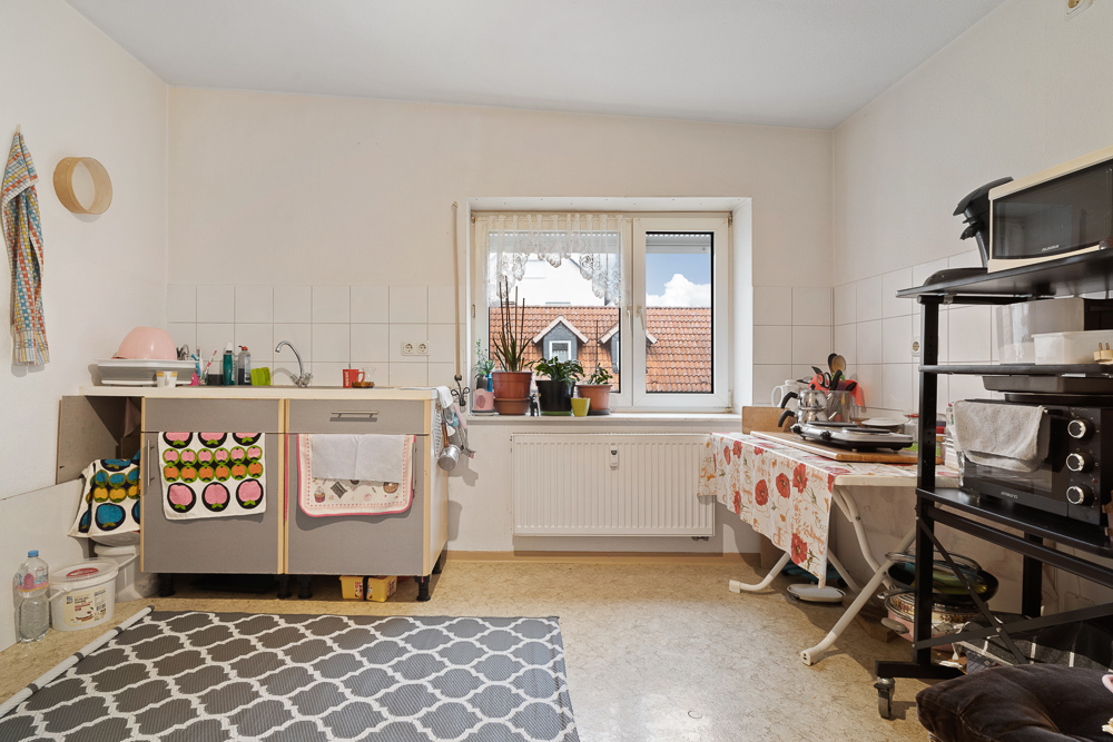 Helle Küche mit Fenster, Spüle, Pflanzen auf der Fensterbank und Küchengeräten auf Regalen.