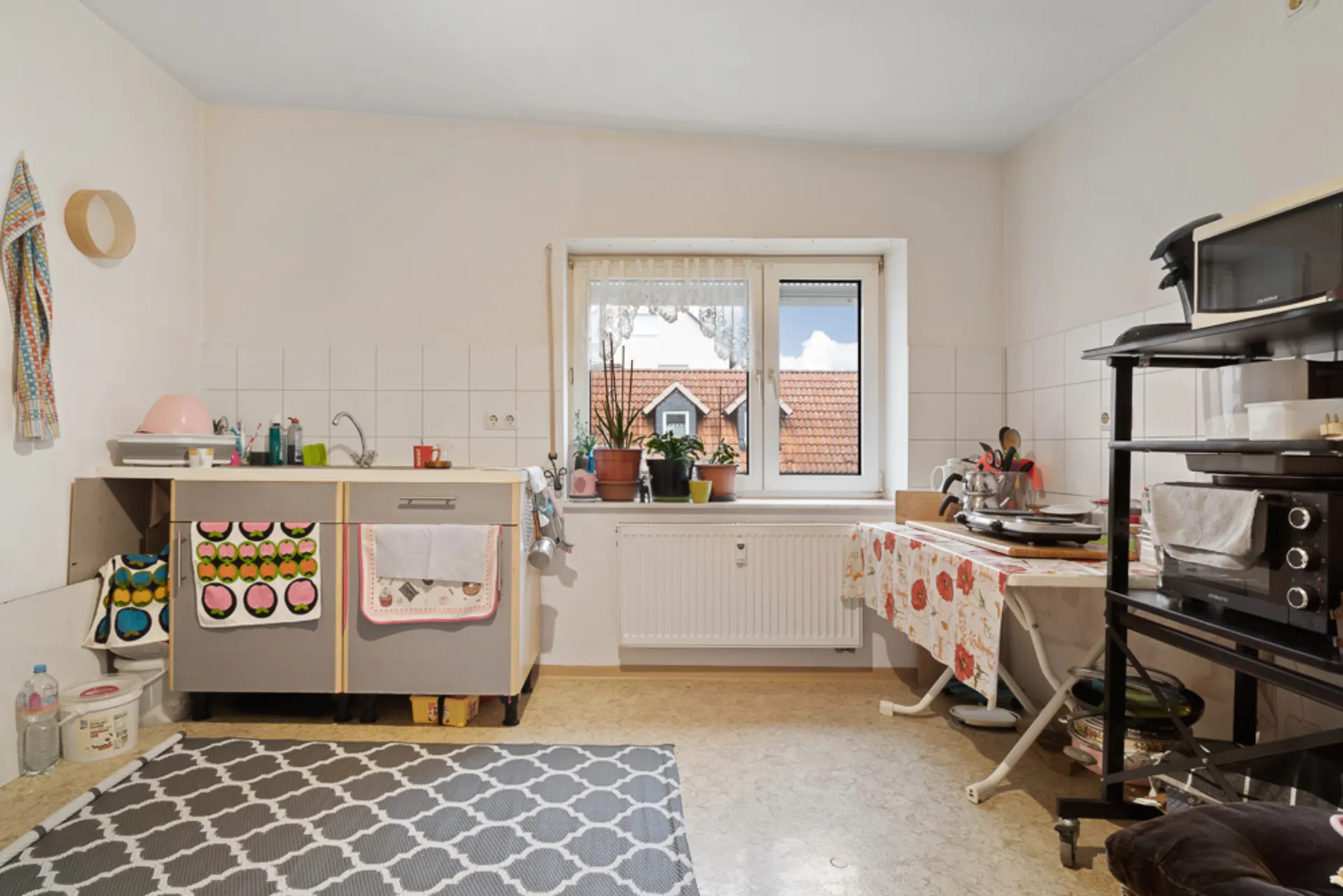 Helle Küche mit Fenster, Spüle, Pflanzen auf der Fensterbank und Küchengeräten auf Regalen.