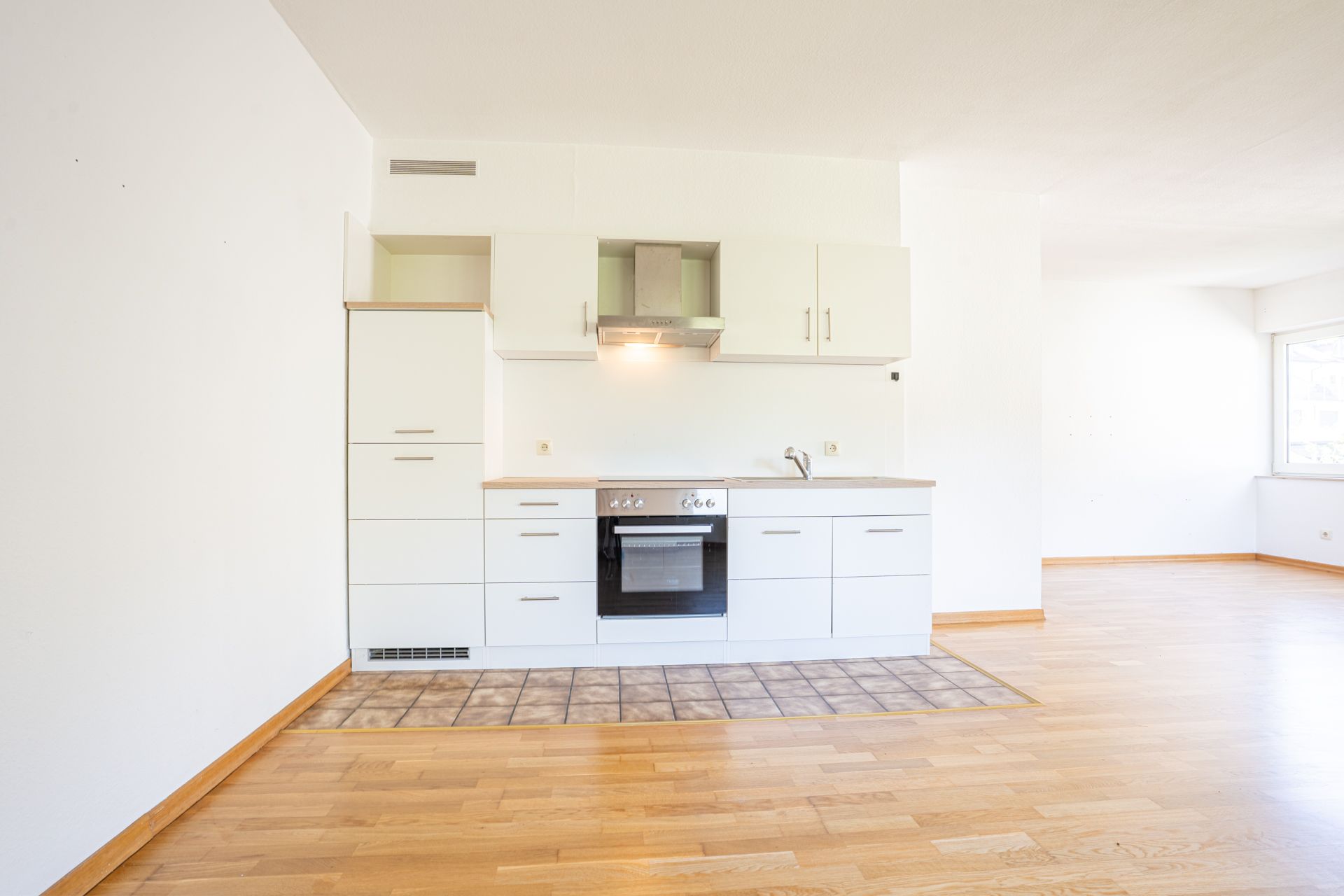 Helle Einbauküche mit weißen Schränken und Herd auf Parkettboden in leerer Wohnung.