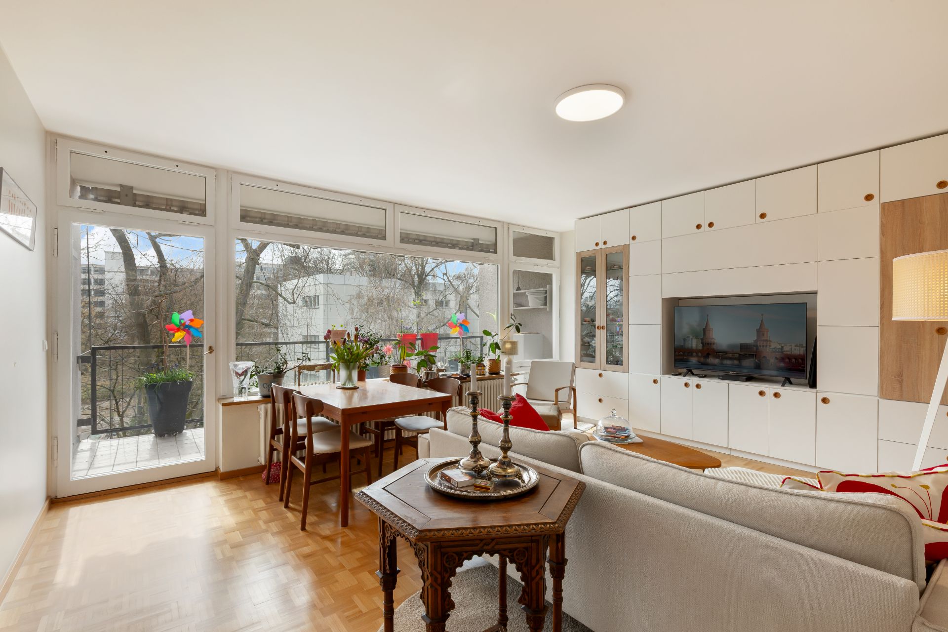 Helles Wohnzimmer mit großem Fenster, Esstisch, Sofa und modernen Einbauschränken.