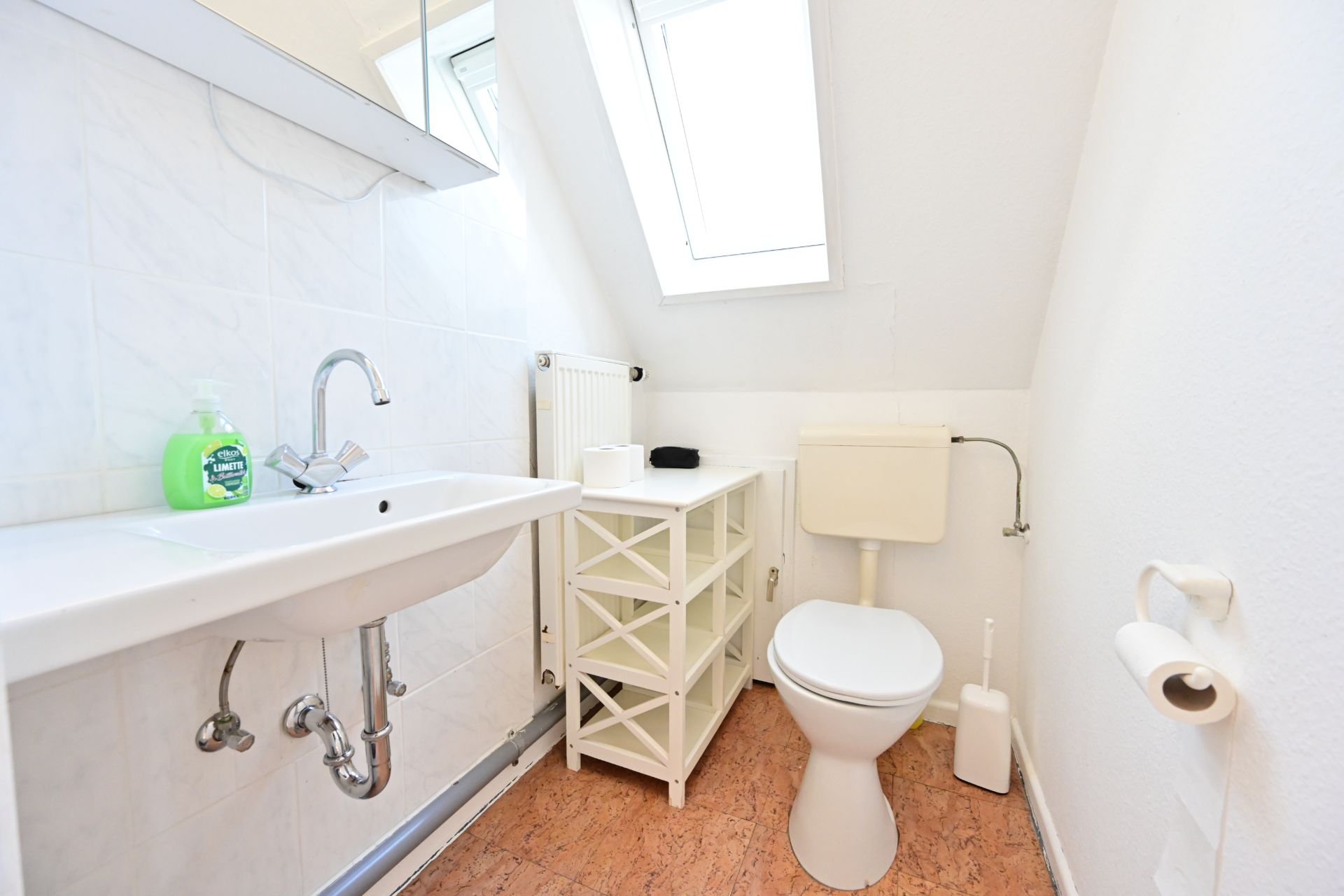 Helles Badezimmer mit Waschbecken, Regal, Toilette und Fenster.