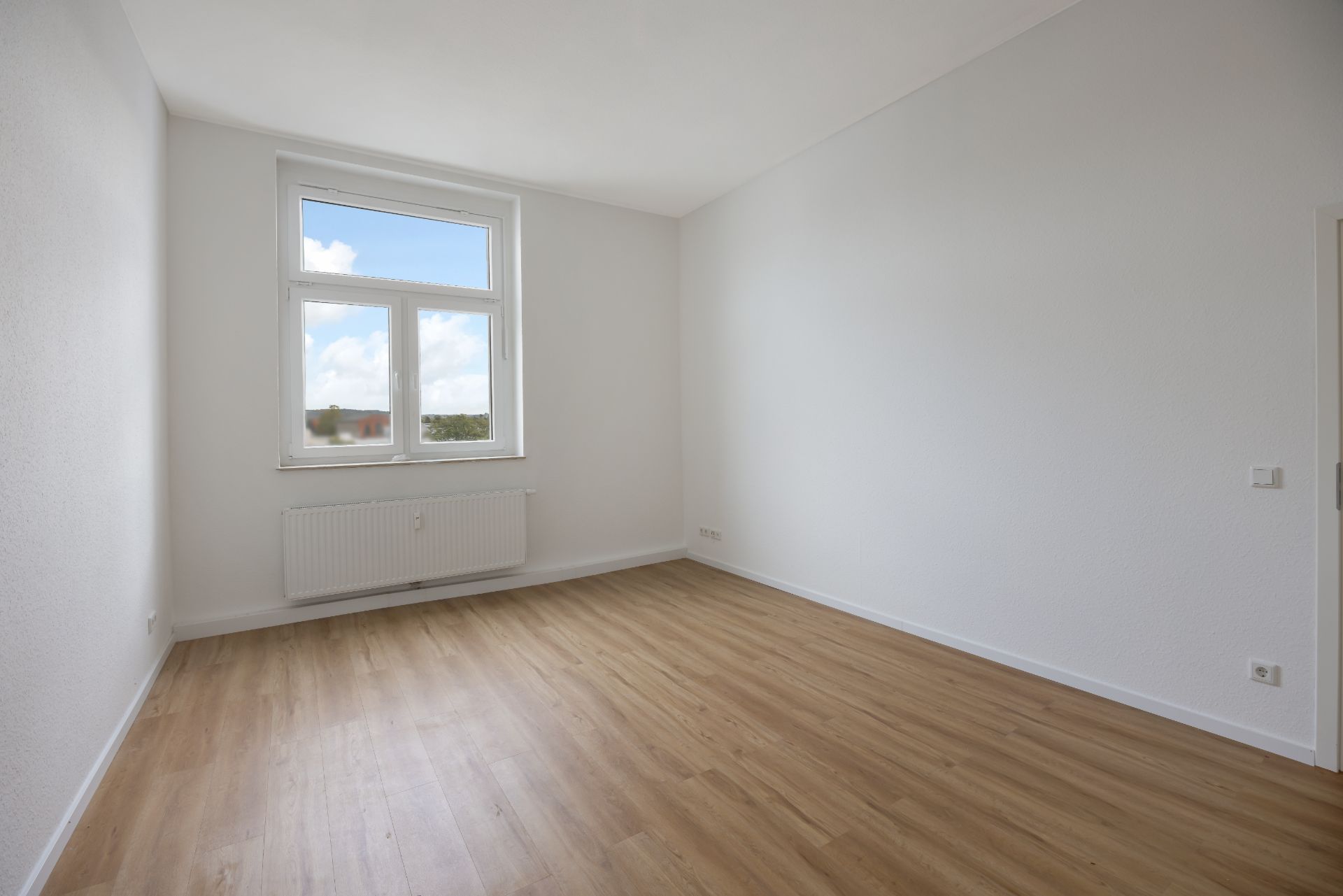 Helles, leeres Zimmer mit Holzboden, weißem Fenster und weiß gestrichenen Wänden.