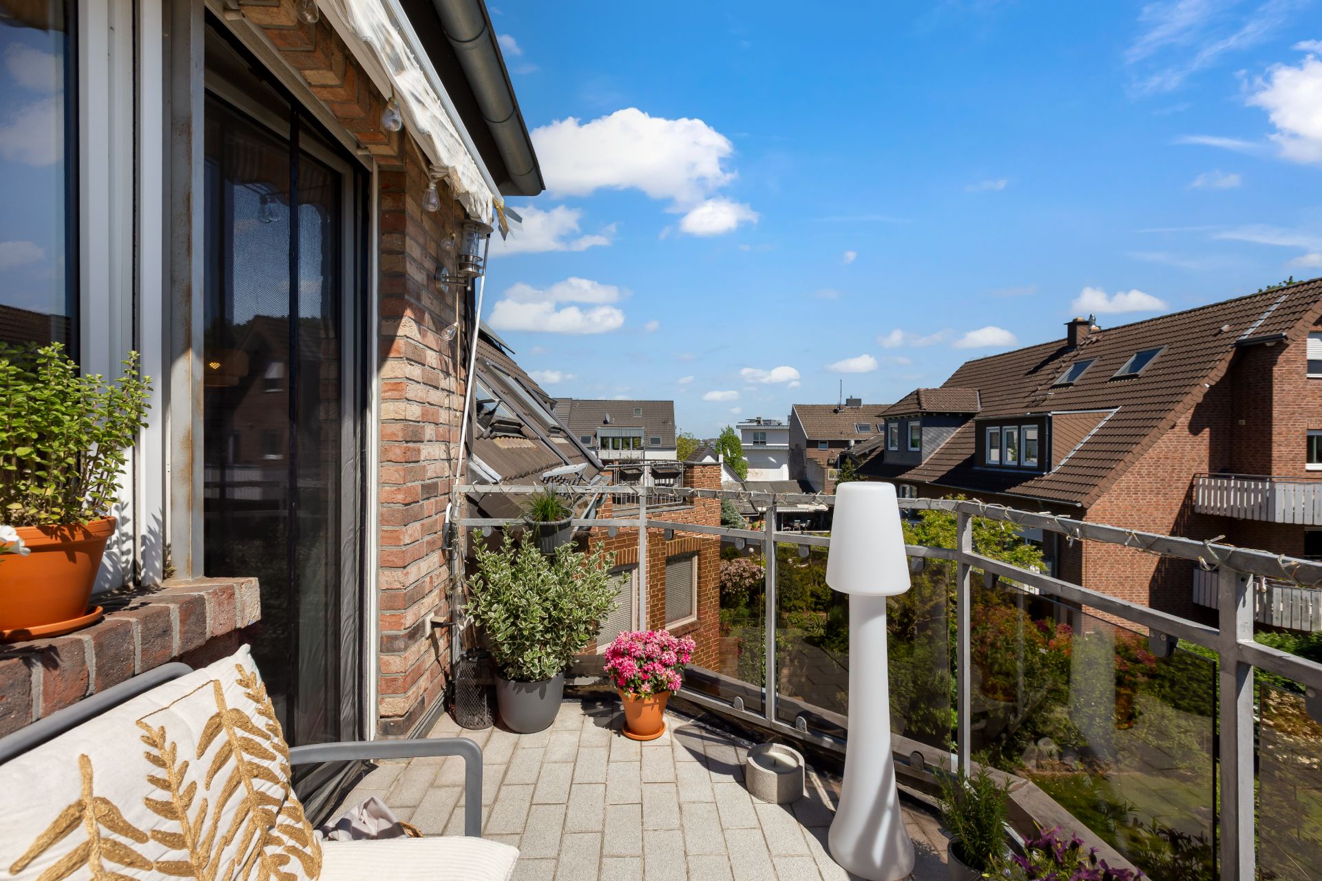 Balkon mit Pflanzen, Sitzbank und Aussicht auf benachbarte Häuser bei sonnigem Wetter.