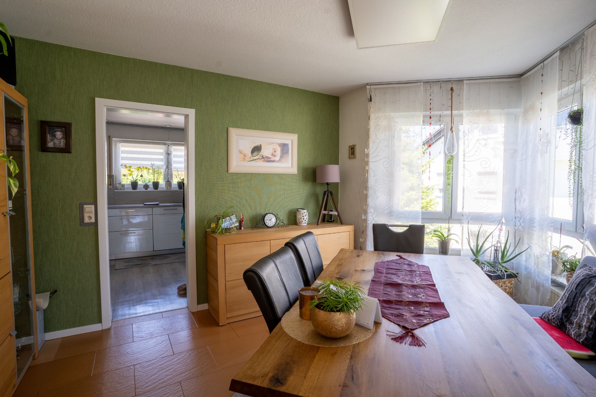 Esszimmer mit Holztisch, Stühlen, Sideboard und großem Fenster mit Pflanzen.
