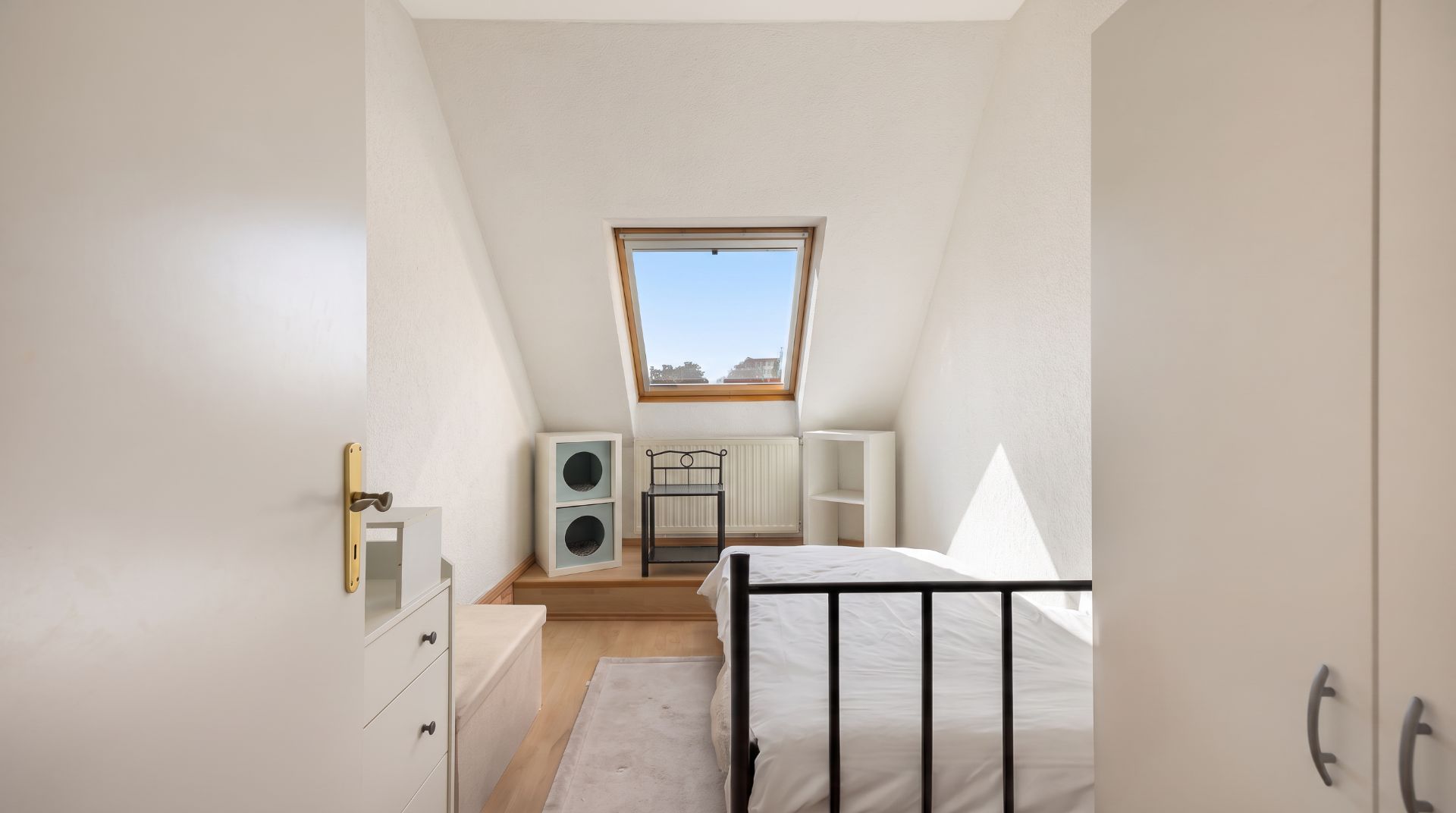 Kleines Schlafzimmer mit Dachfenster, Bett, weißen Möbeln und Holzfußboden.