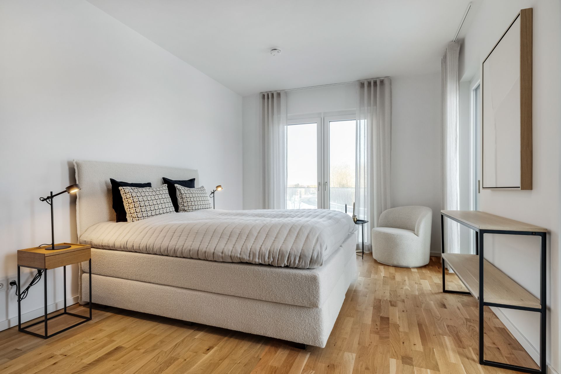 Modernes Schlafzimmer mit Doppelbett, Nachttischen, Sessel und Fenster mit Vorhängen.