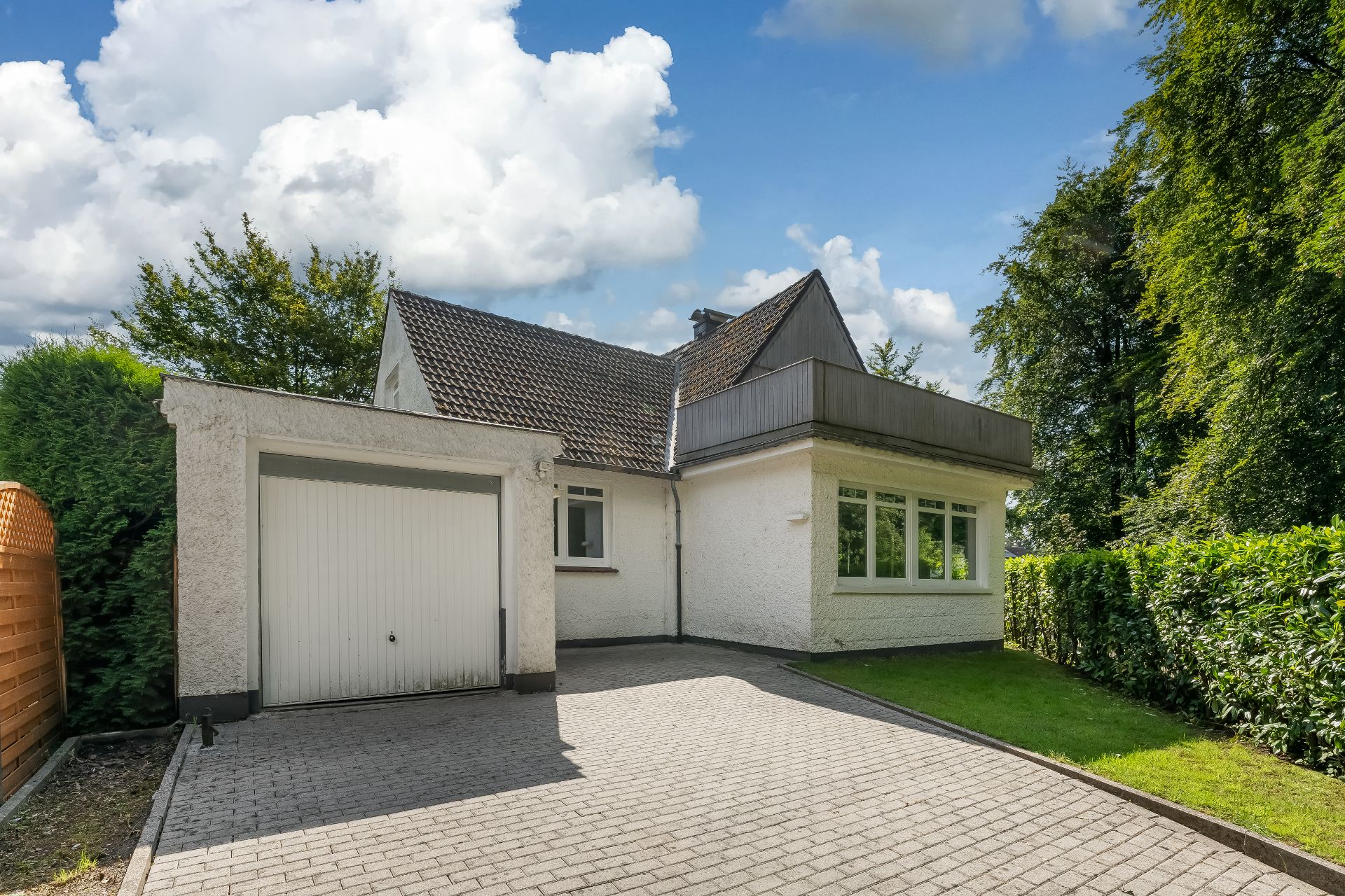 Weißes Einfamilienhaus mit Garage, gepflasterter Einfahrt und Vorgarten mit Hecke.