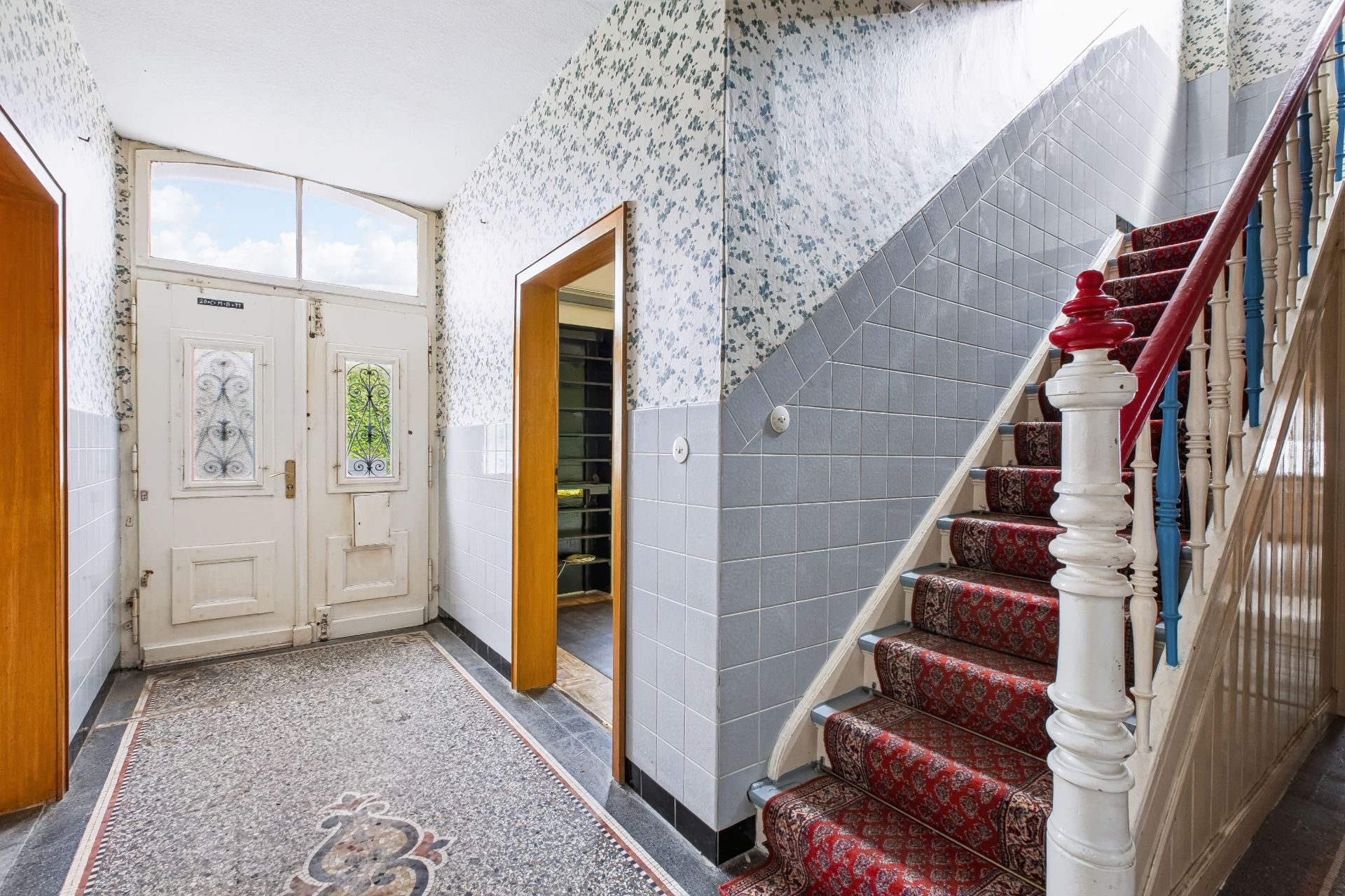 Heller Flur mit Teppichtreppe, gemusterten Wänden und weißer Eingangstür in einem Wohnhaus.