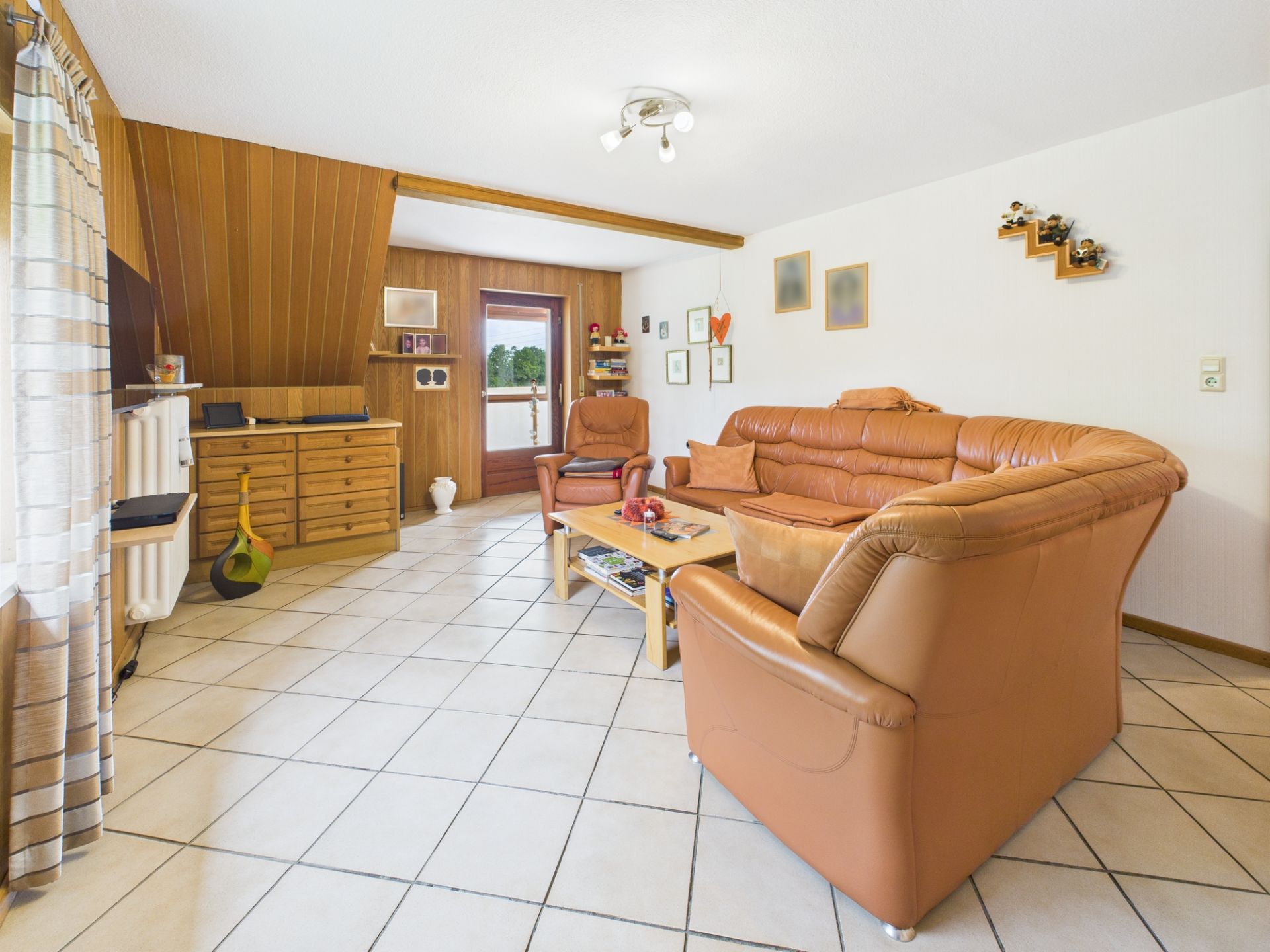 Wohnzimmer mit hellbraunen Ledersofas, Couchtisch und Holzmöbeln auf gefliestem Boden.