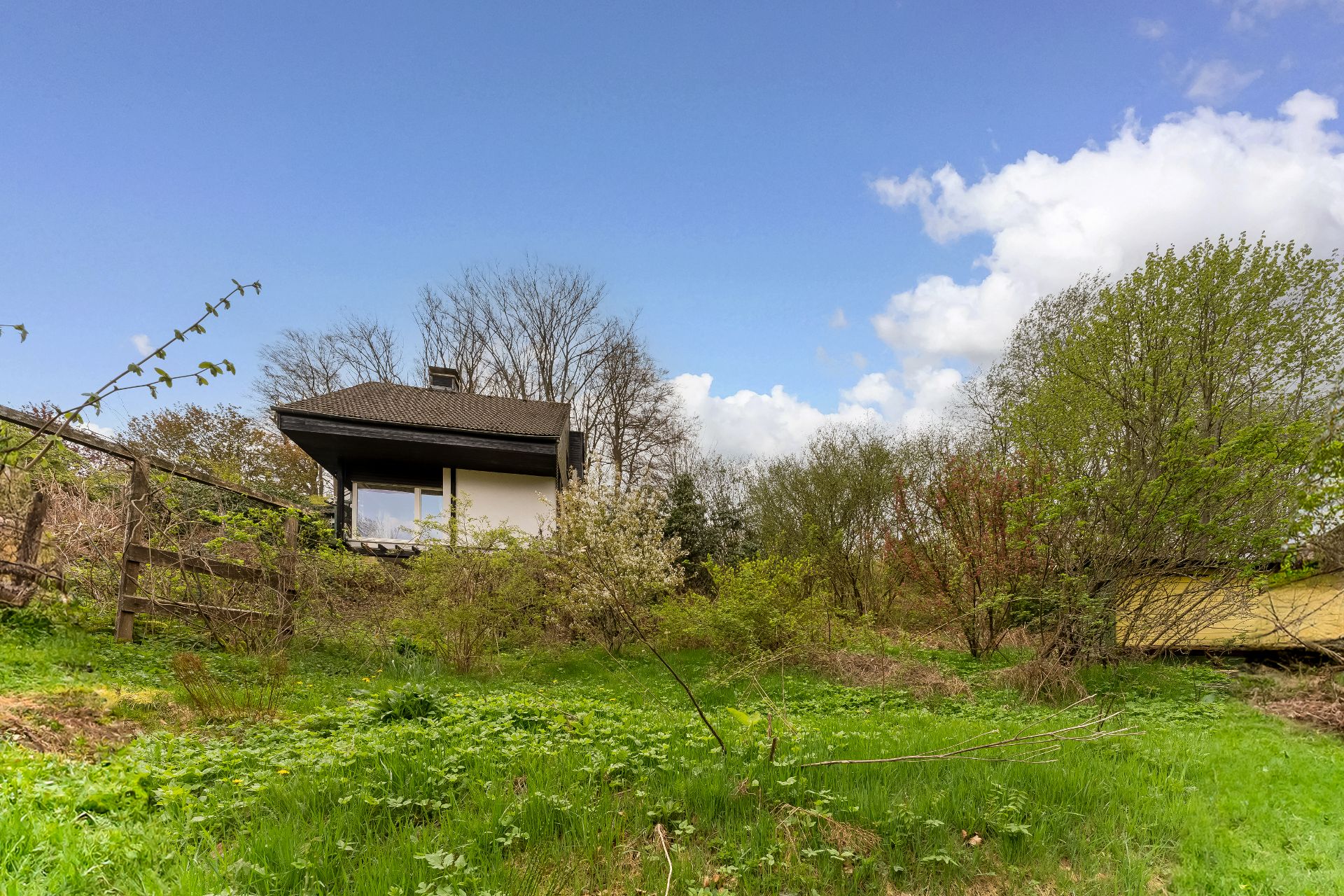 Ein kleines Haus mit dunklem Dach inmitten von grünem, bewachsenem Garten.