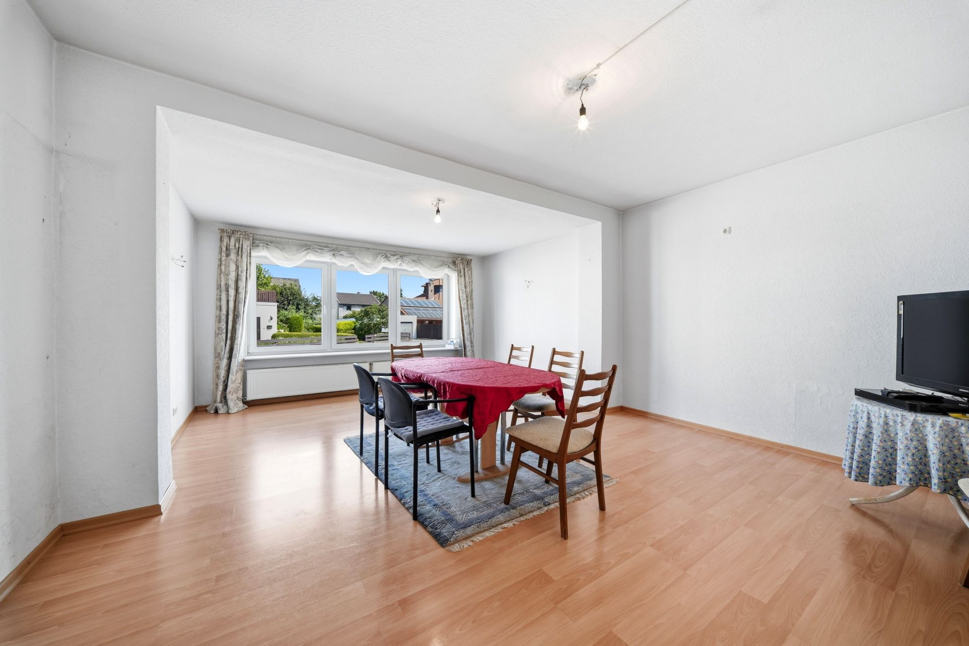 Helles Wohnzimmer mit Esstisch, Stühlen, Laminatboden und großem Fenster mit Blick nach draußen.