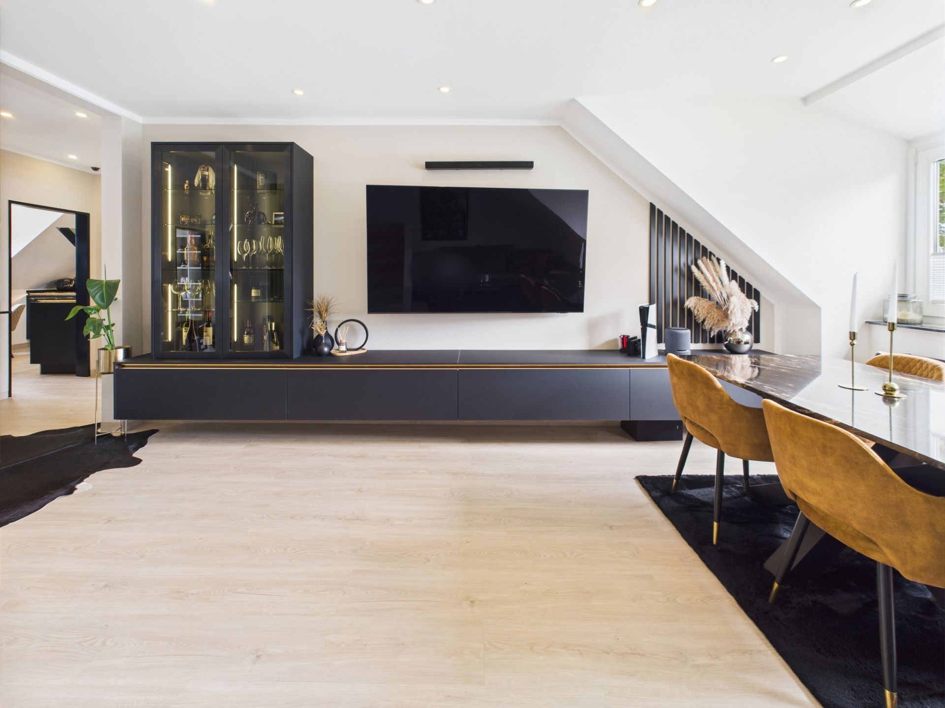 Modernes Wohnzimmer mit großem Fernseher, dunklem Schrank und Esstisch mit vier Stühlen.