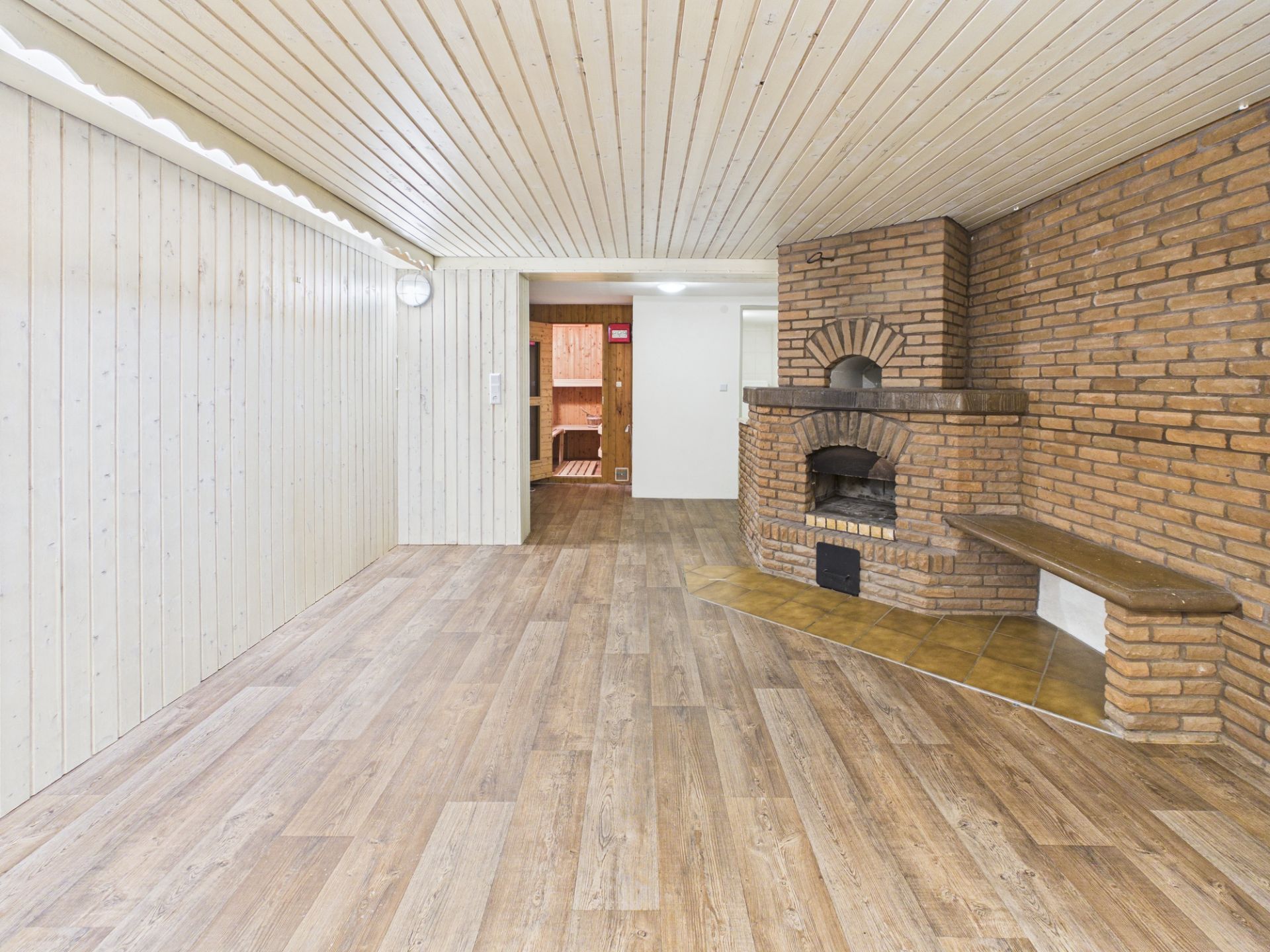 Heller Raum mit Holzdecke, Parkettboden und gemauertem Kamin in der Ecke.