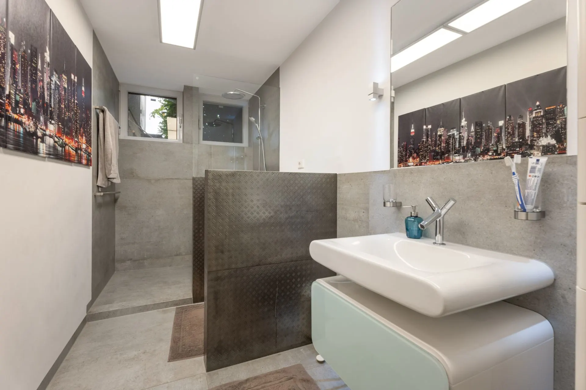 Modernes Badezimmer mit Waschbecken, begehbarer Dusche und Wandbildern einer Skyline.
