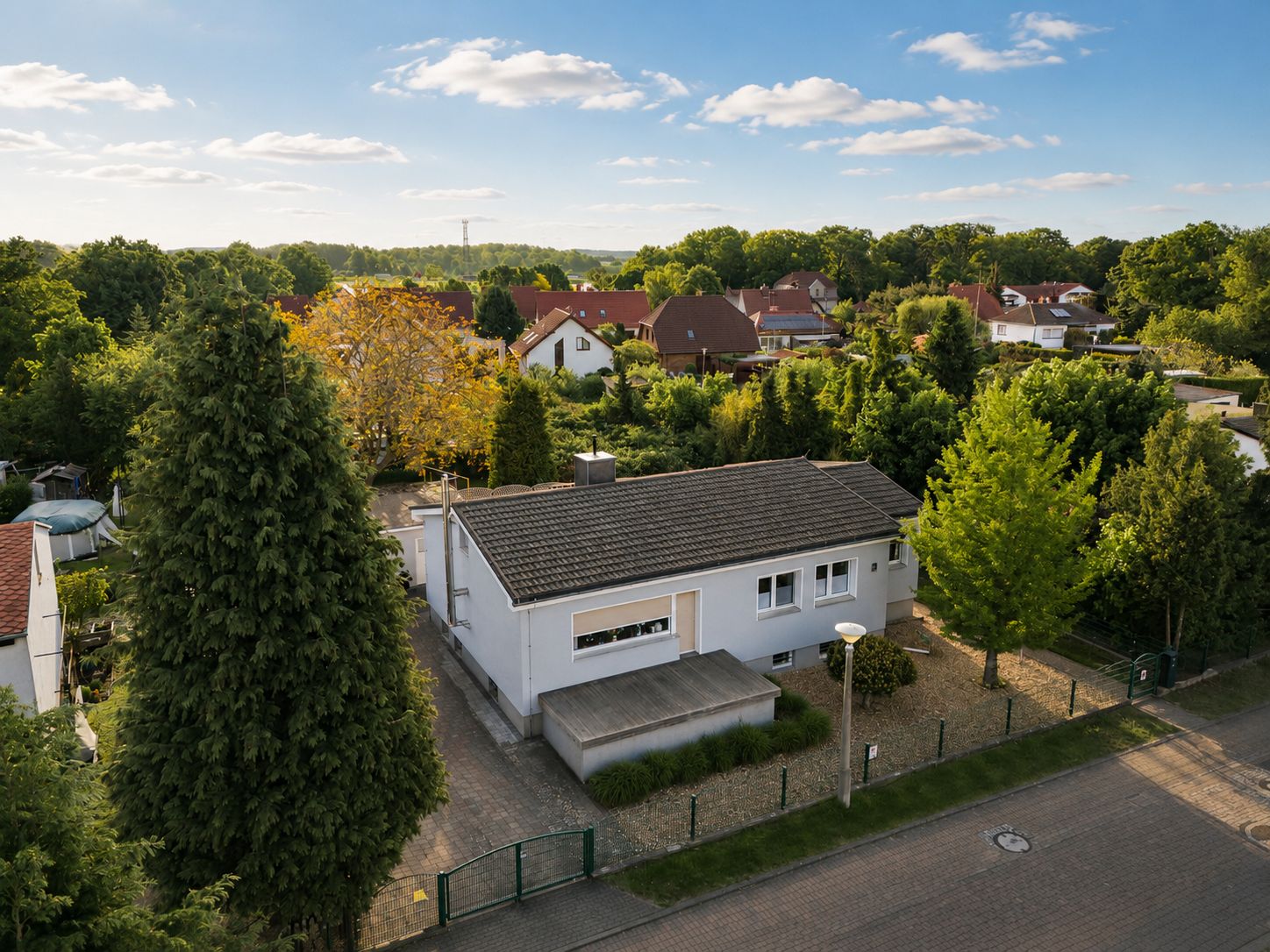 Luftaufnahme eines weißen Einfamilienhauses mit Garten und Einfahrt in einer Wohngegend.
