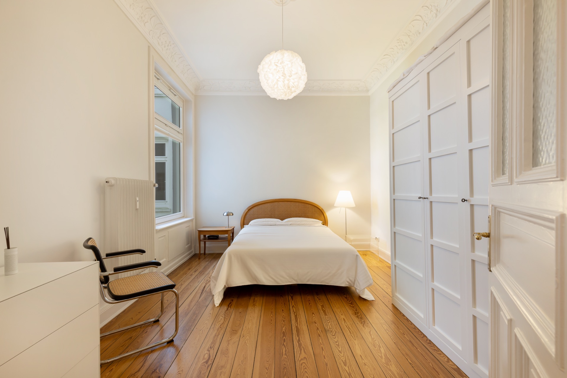 Helles Schlafzimmer mit Doppelbett, Holzfußboden, weißen Wänden und großem Einbauschrank.