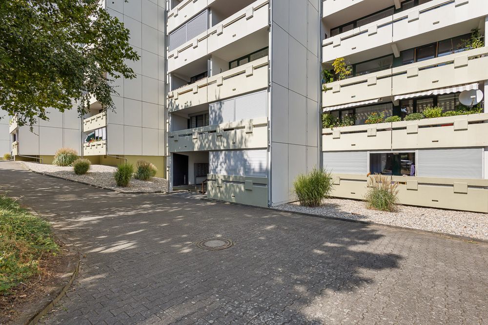 Mehrfamilienhaus mit Balkonen, geschlossenen Rollläden und bepflanztem Vorgarten.