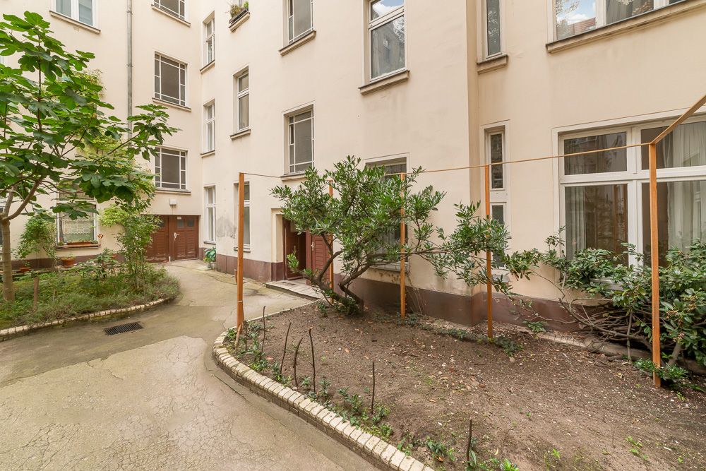 Heller Innenhof mit Pflanzenbeeten, Bäumen und mehreren Fenstern einer Wohnanlage.