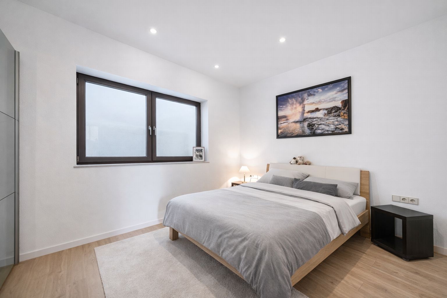 Helles Schlafzimmer mit Doppelbett, großem Fenster und Wandbild.