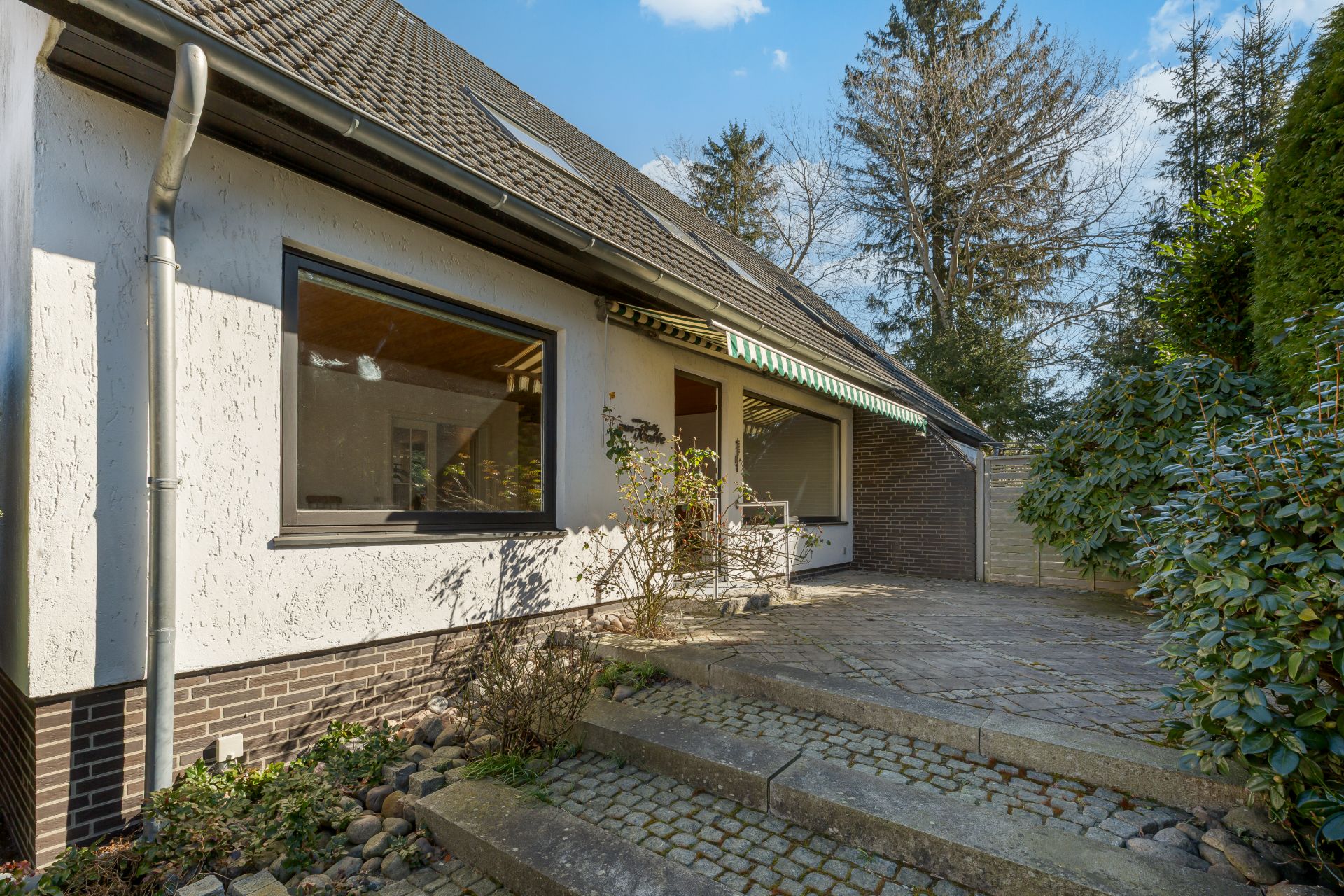 Haus mit weißer Fassade, großer Fensterfront und gepflasterter Terrasse mit Garten.