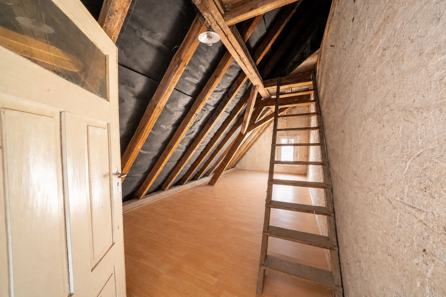 Dachbodenraum mit Holzboden, offener Tür und Holztreppe unter sichtbaren Balken.