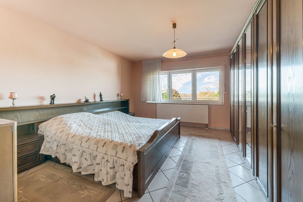 Helles Schlafzimmer mit großem Bett, Holzmöbeln und Fenster mit Blick nach draußen.