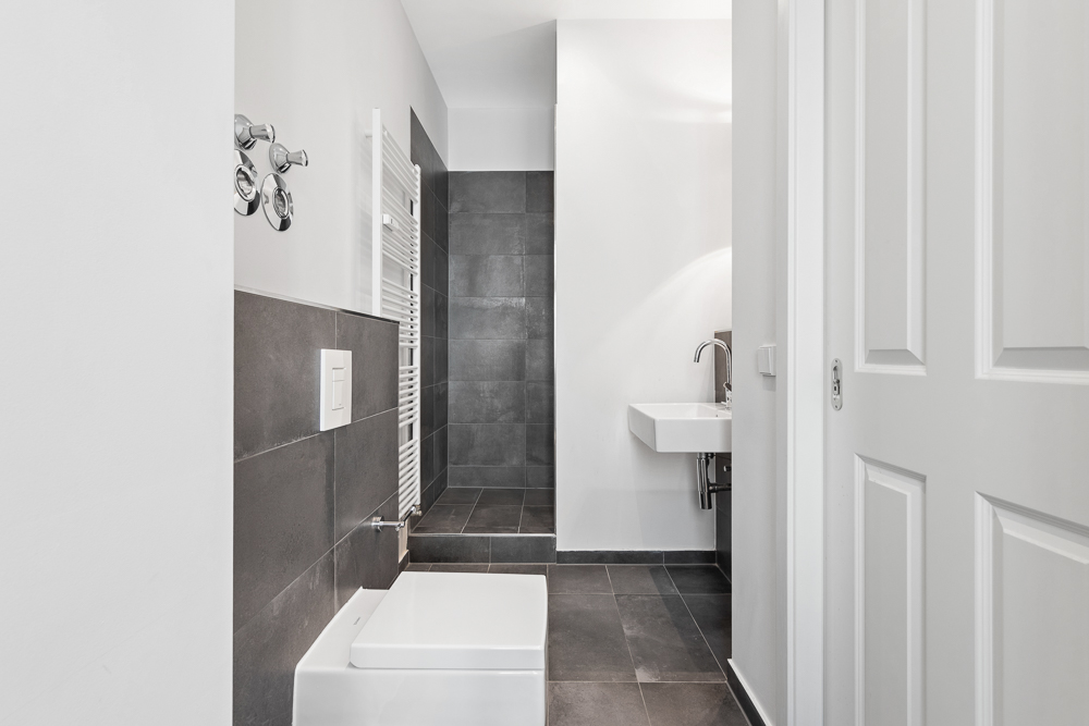 Modernes Bad mit dunklen Fliesen, Toilette, Waschbecken und offener Dusche.
