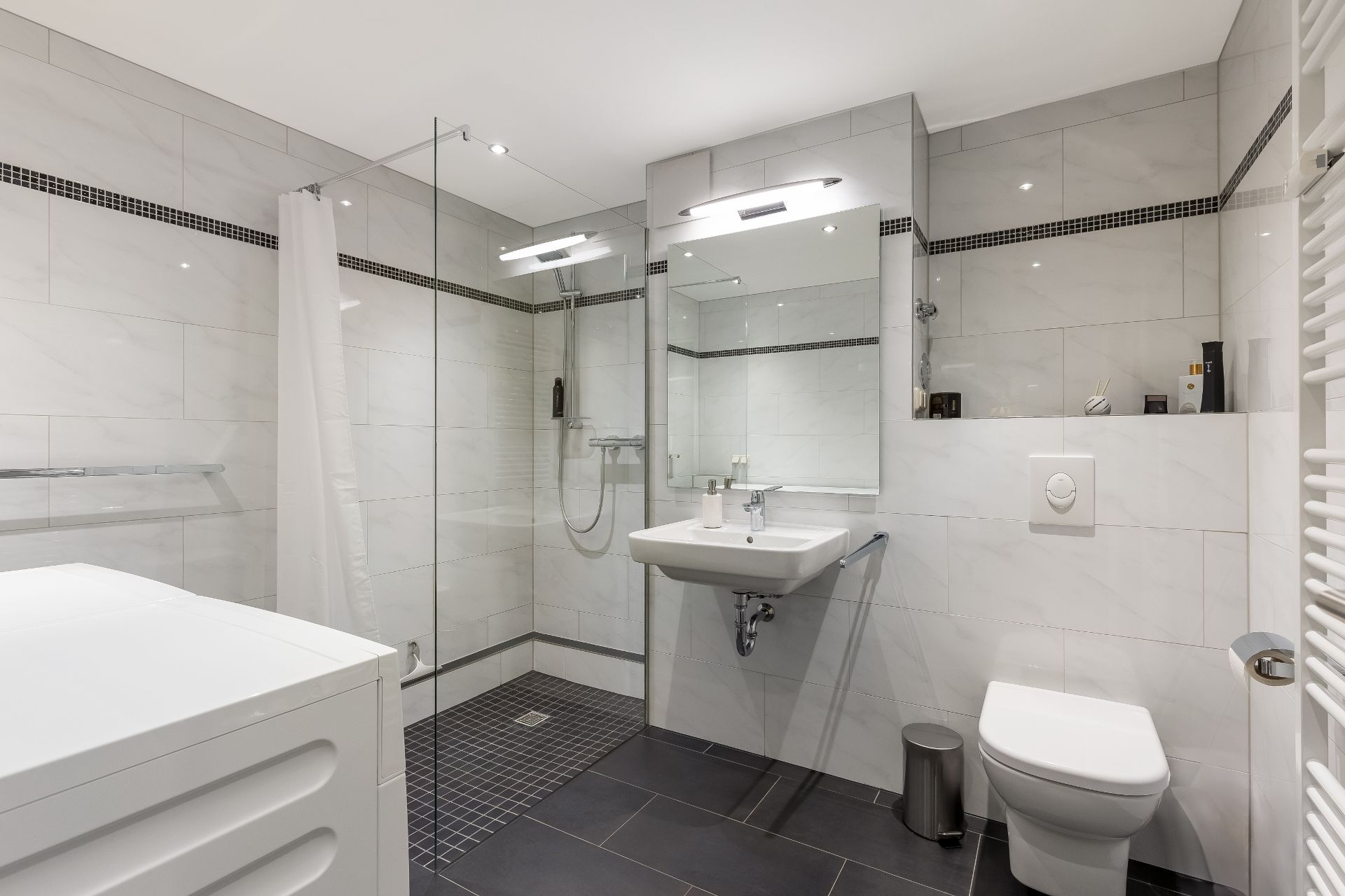 Modernes Badezimmer mit ebenerdiger Dusche, Waschbecken, WC und Waschmaschine.