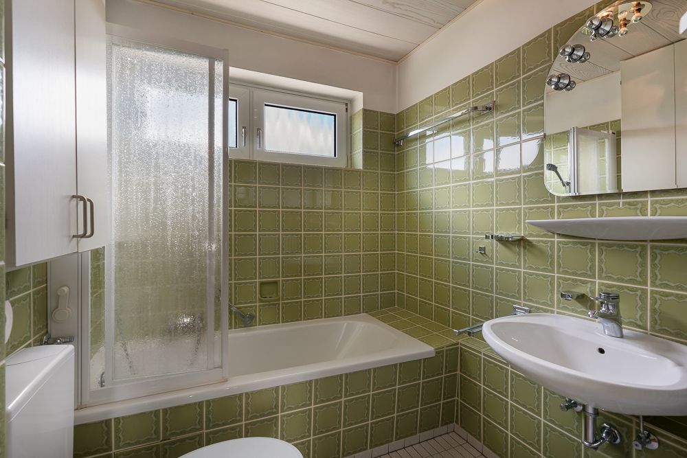 Kleines Badezimmer mit grünen Fliesen, Badewanne, Waschbecken und Spiegel.
