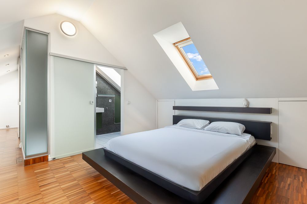 Modernes Schlafzimmer mit Dachfenster, großem Bett und Holzfußboden.