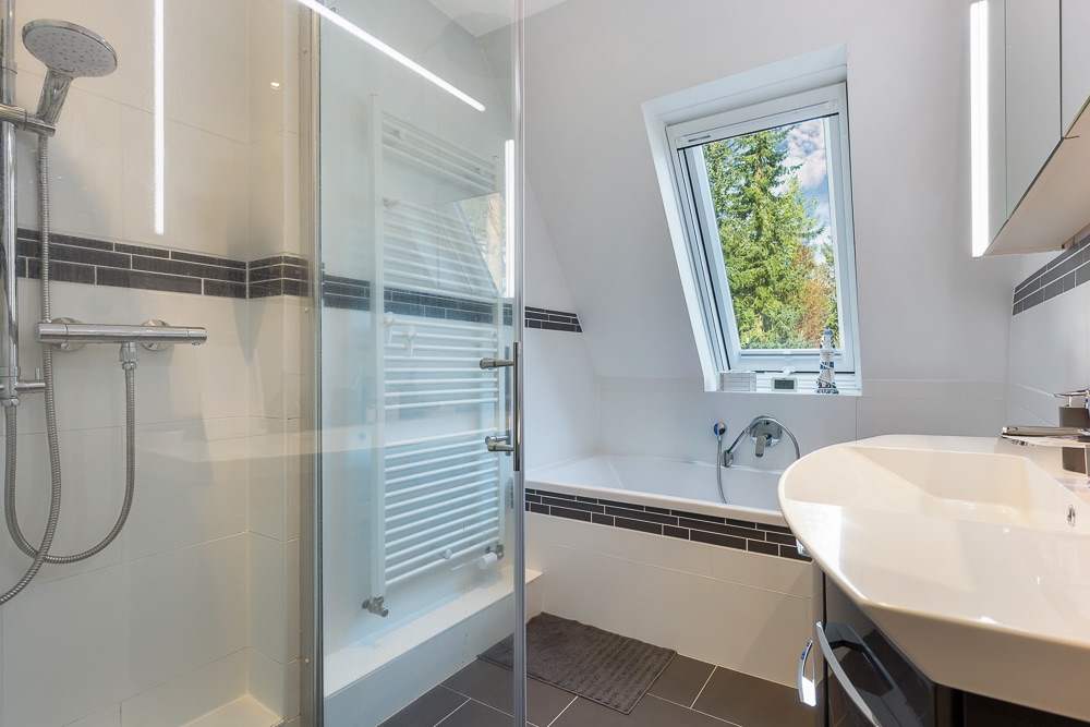 Modernes Badezimmer mit Dusche, Badewanne und großem Fenster mit Blick ins Grüne.