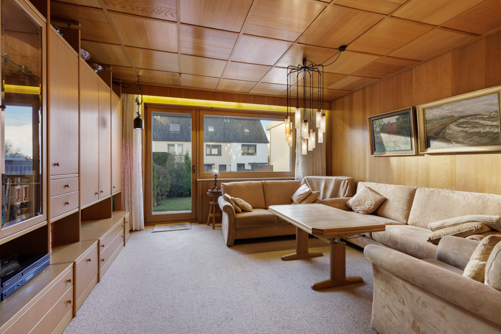 Wohnzimmer mit Holzwänden, Sofagarnitur, Couchtisch, großem Fenster und Hängelampen.