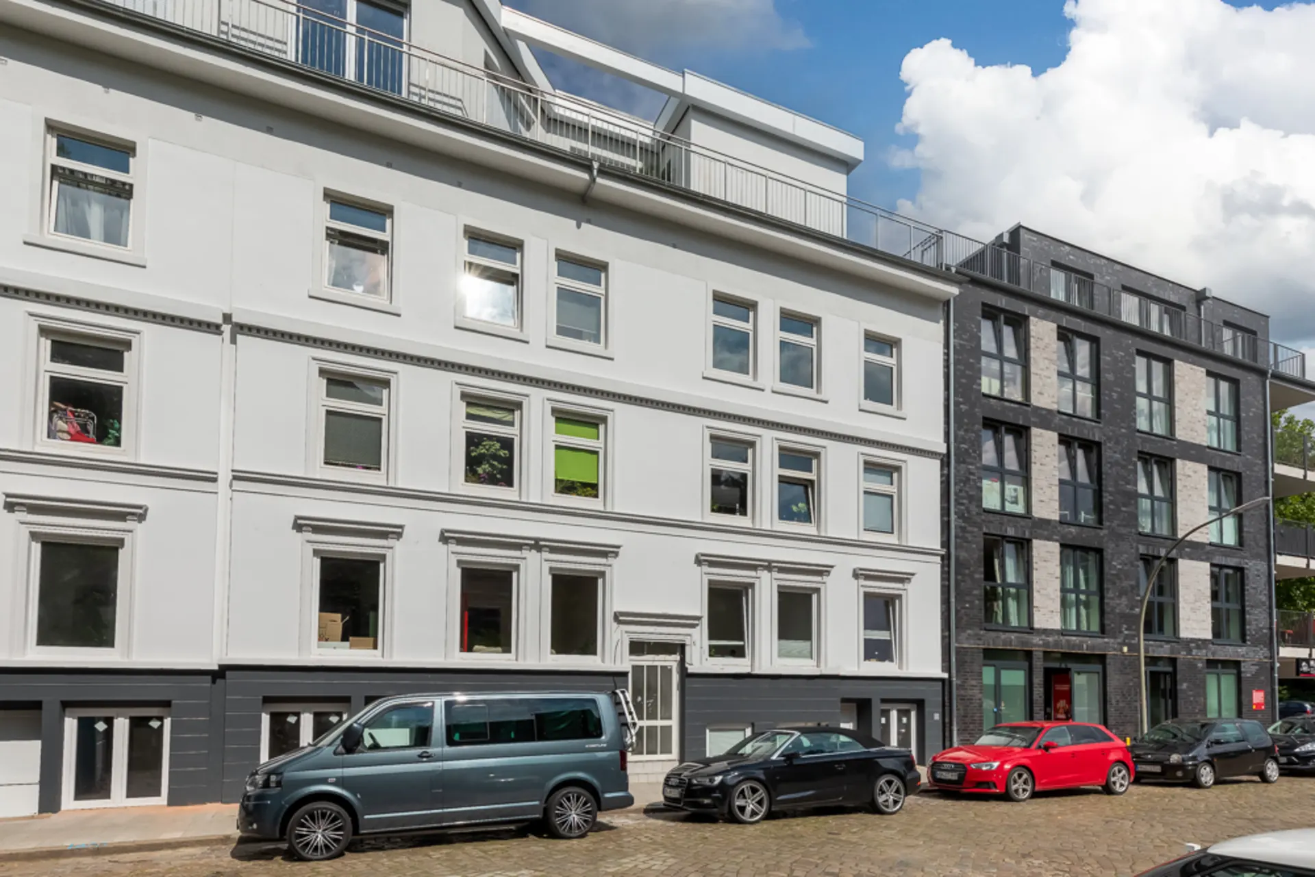 Fassade eines modernen Wohnhauses mit mehreren Fenstern und geparkten Autos davor.