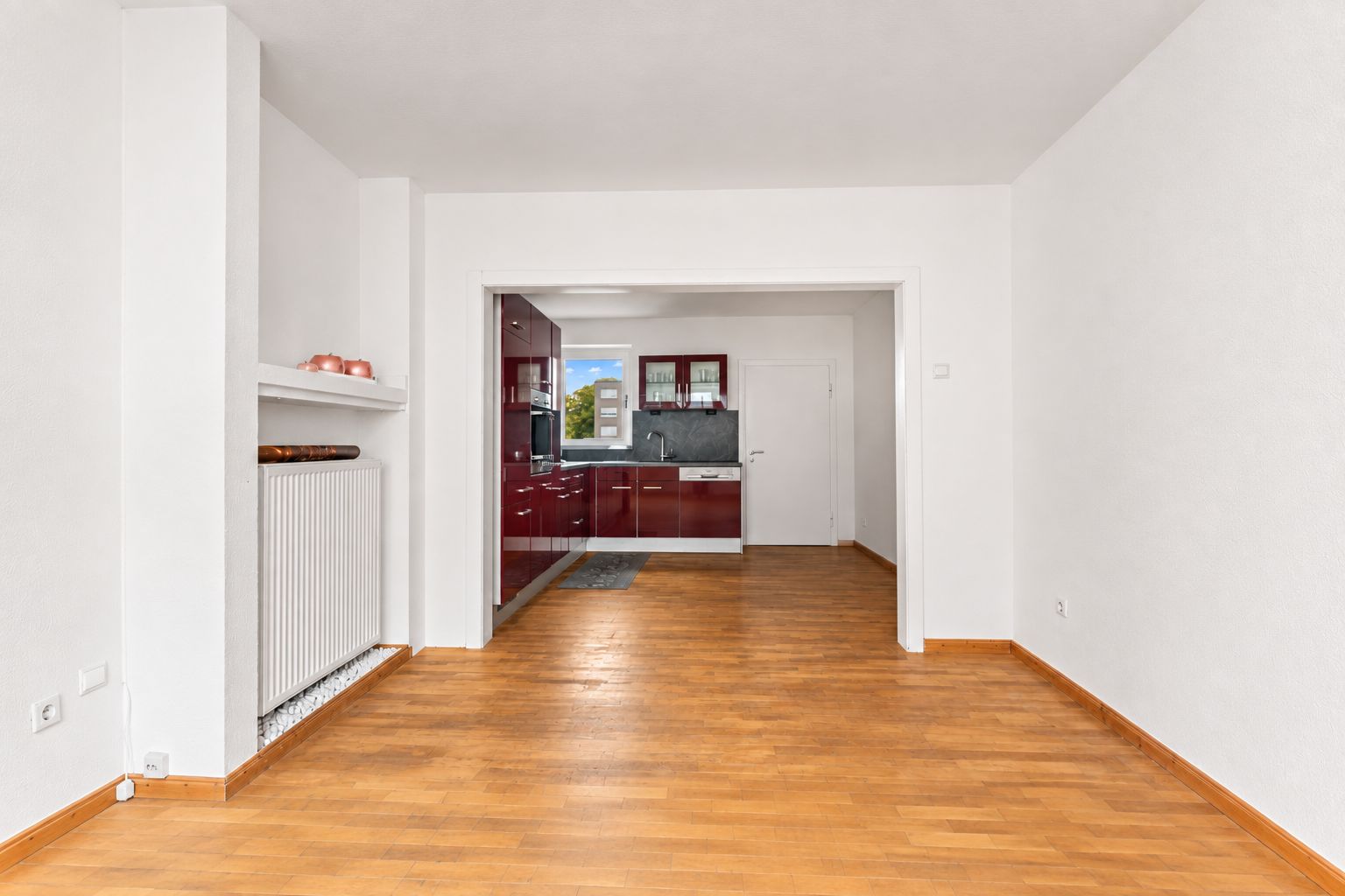 Helles Wohnzimmer mit Holzfußboden und Blick auf eine offene Küche mit roten Schränken.