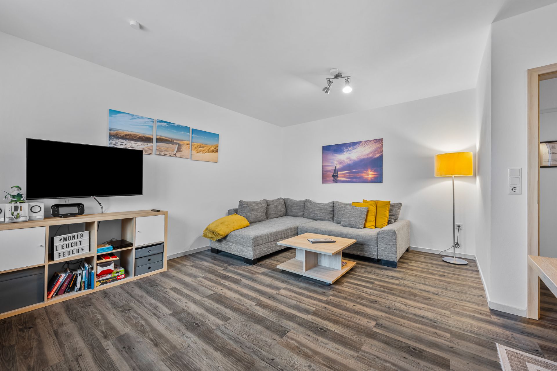 Modernes Wohnzimmer mit grauem Ecksofa, Couchtisch, Fernseher und Stehlampe auf Holzfußboden.