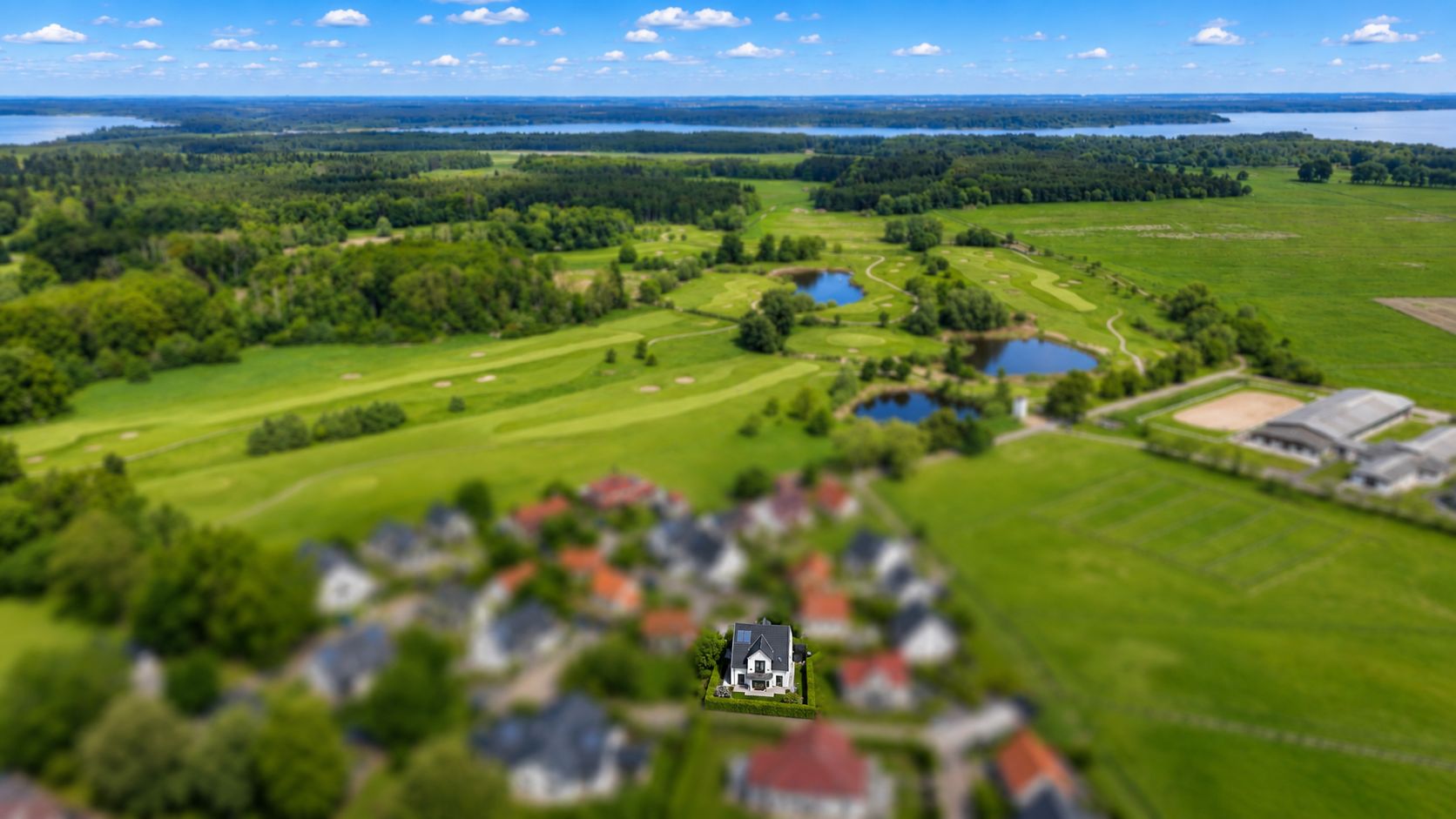 Landschaft mit Häusern im Vordergrund, Feldern, Bäumen und mehreren Seen im Hintergrund.