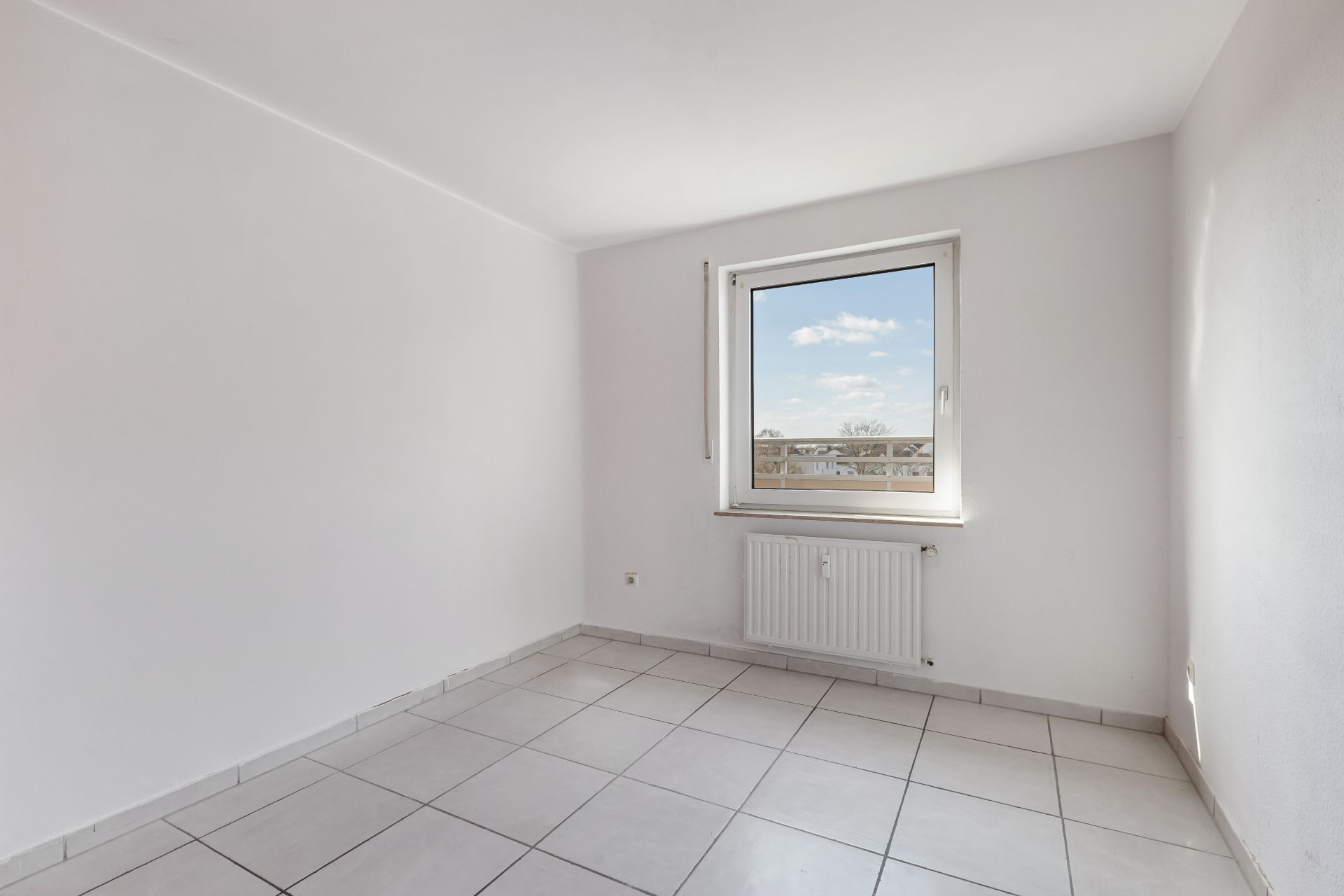 Leeres Zimmer mit weißen Wänden, Fliesenboden, Fenster und Heizung.