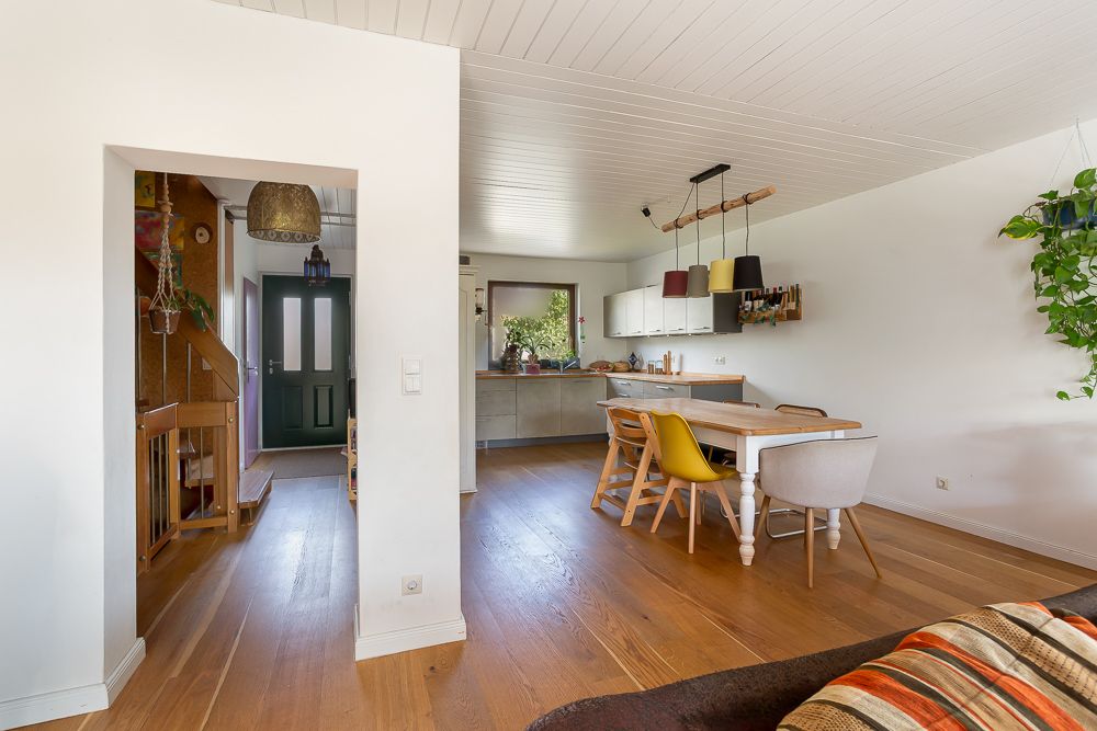 Heller Wohnbereich mit Esstisch, vier Stühlen, Holzboden und Blick auf Küche und Treppe.