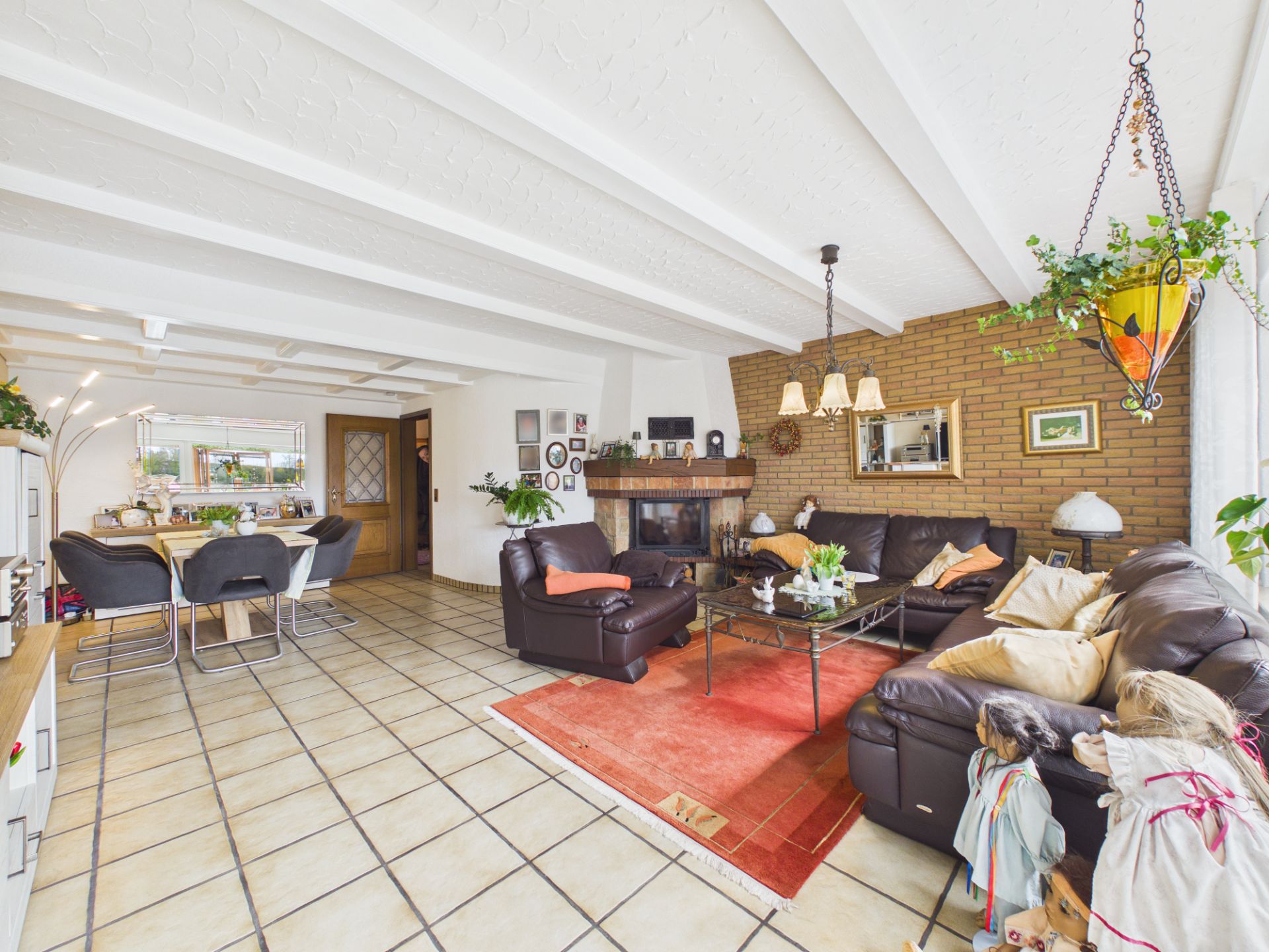 Wohnzimmer mit braunen Ledersofas, Kamin, Esstisch und vielen Pflanzen.