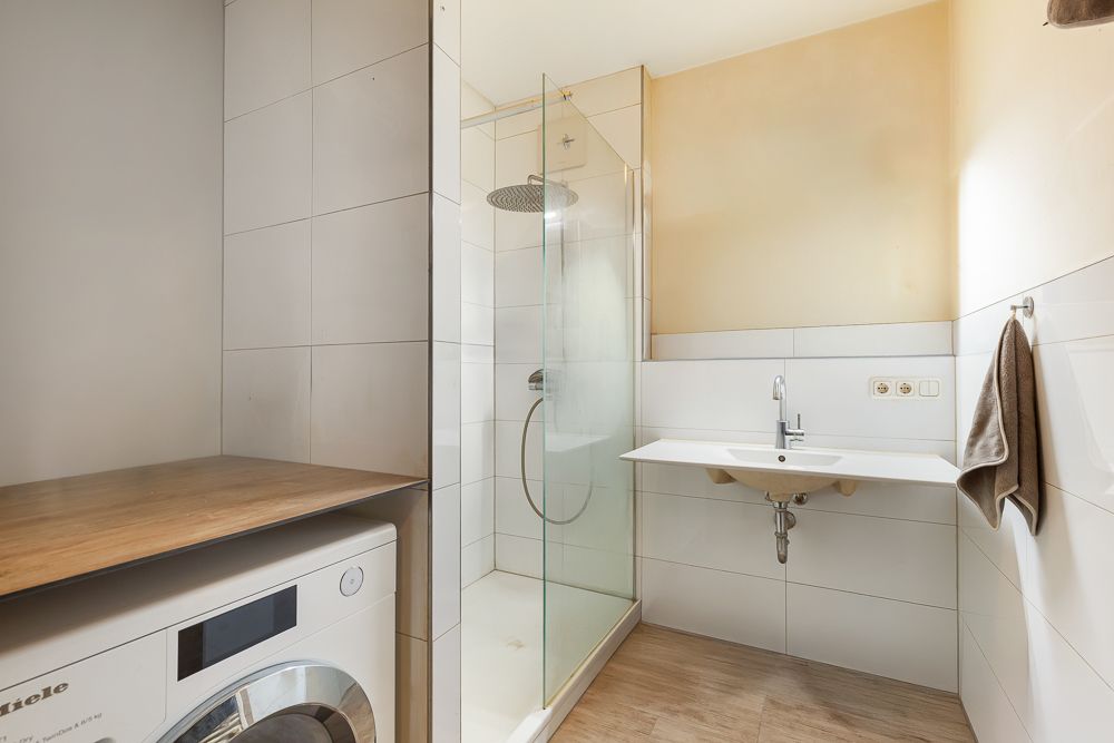Modernes Badezimmer mit Dusche, Waschbecken, Handtuch und Waschmaschine.