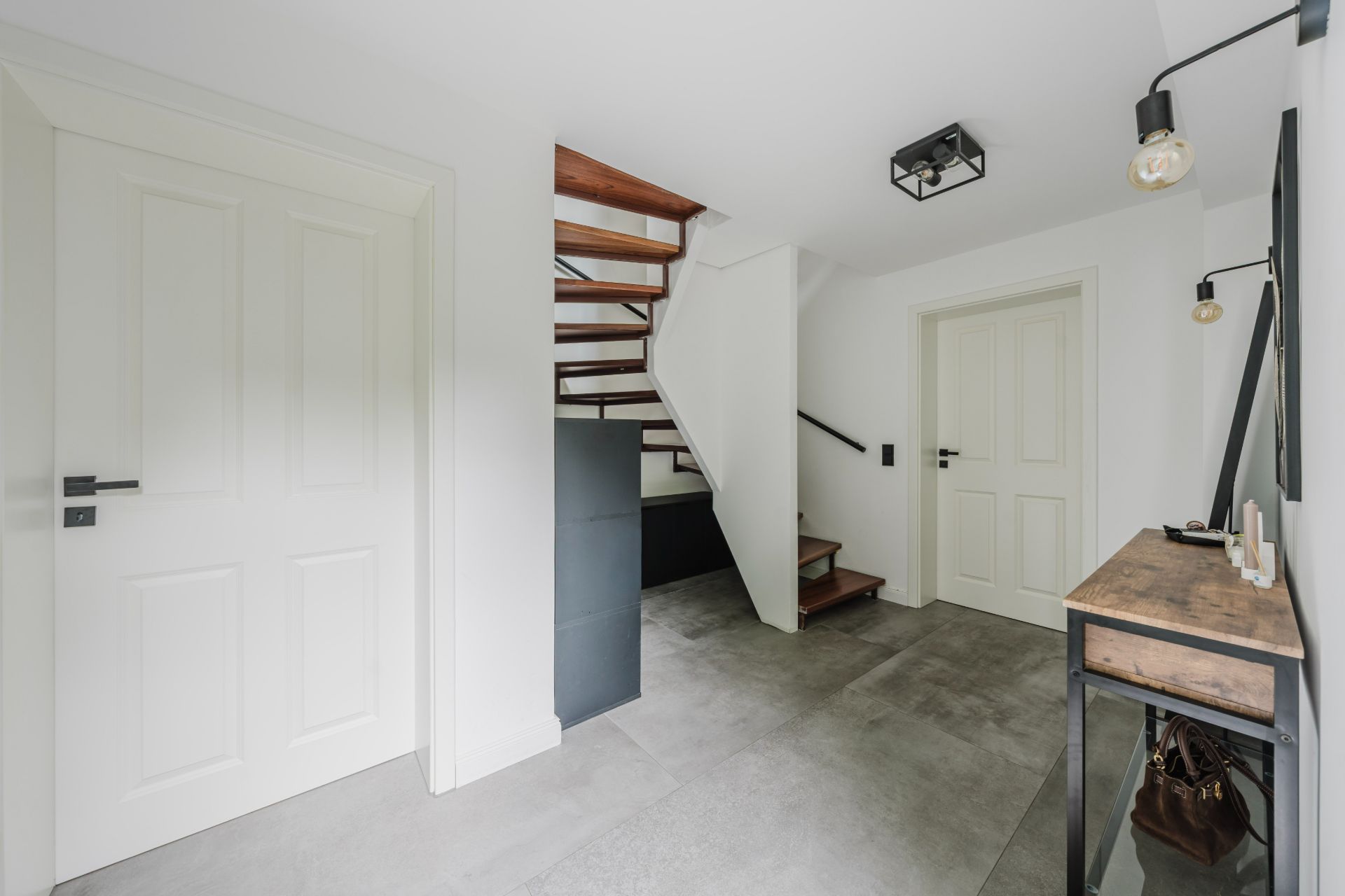 Heller Flur mit zwei weißen Türen, Treppe aus Holz und modernem Konsolentisch.