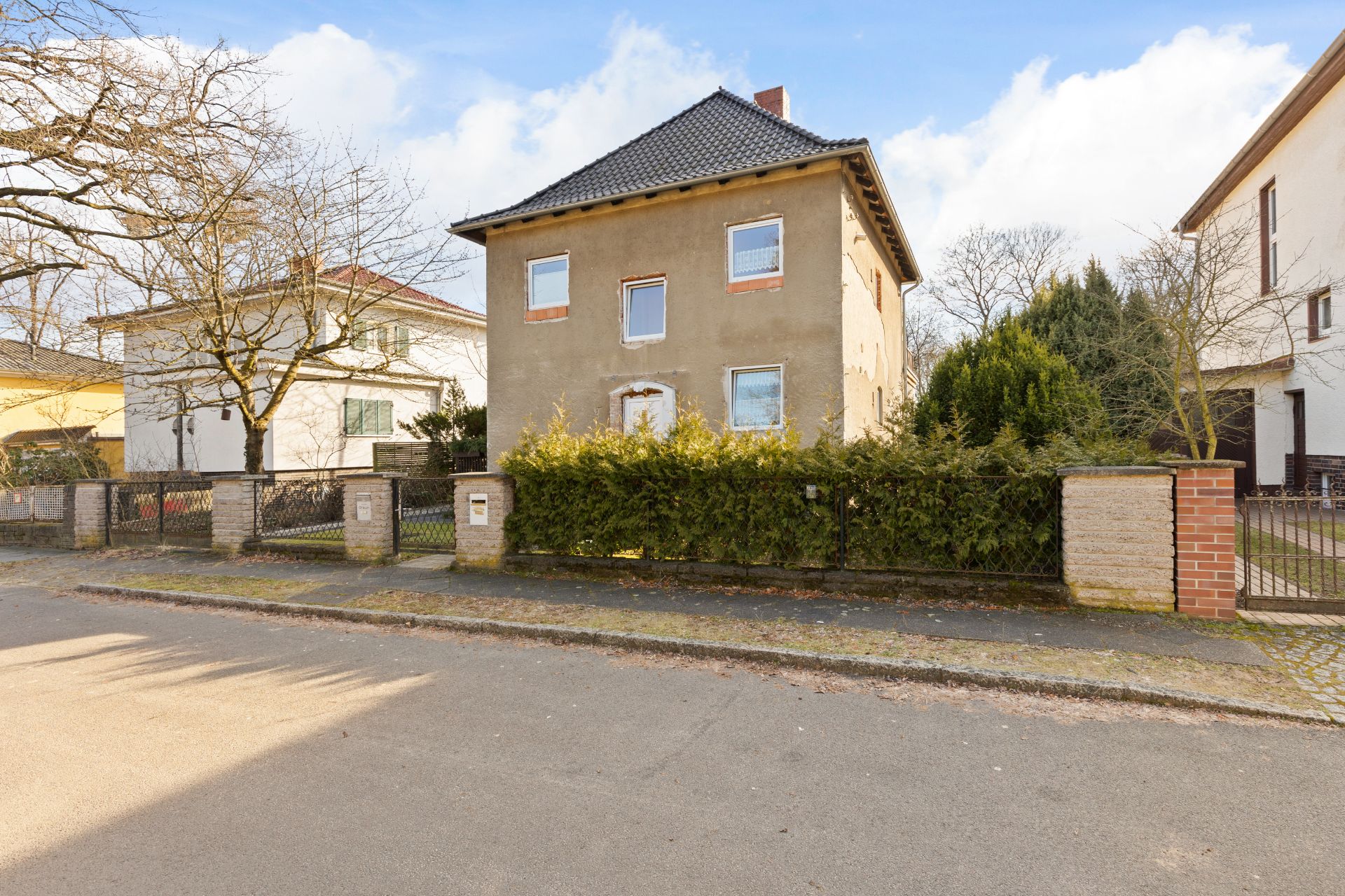 Ein zweistöckiges Wohnhaus mit Zaun und Hecke, aufgenommen von der Straße.